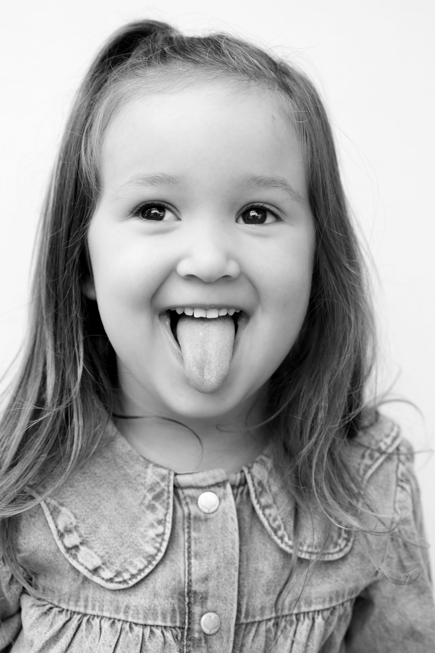 A playful sequence of four black and white portraits showing a child in denim making silly faces and sticking out their tongue.