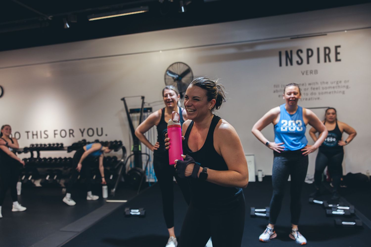 Fitness enthusiasts participate in a high-energy group workout class at an indoor gym with Inspire branding.