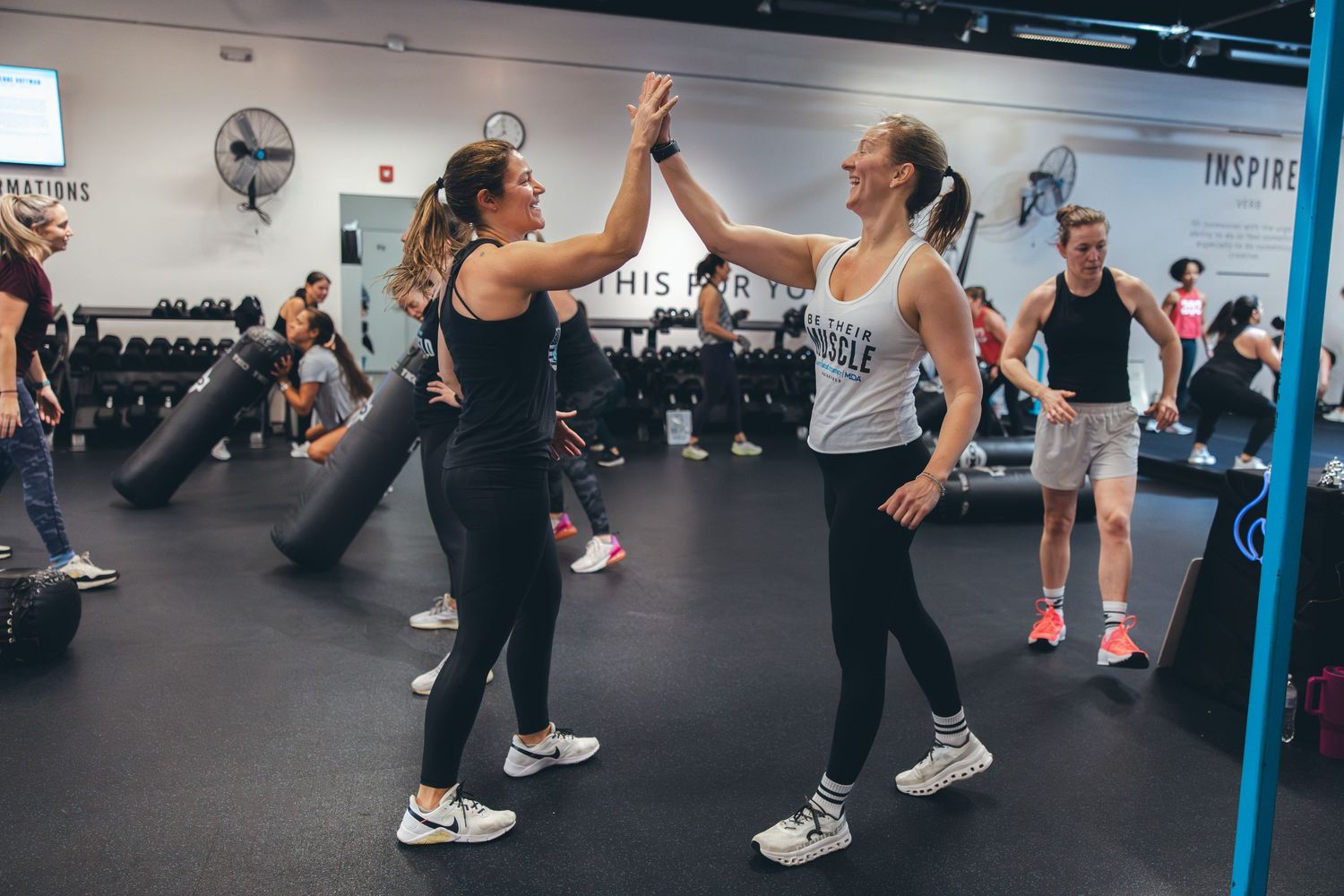 Two athletes celebrate with a high-five during a group workout session in a fitness studio.