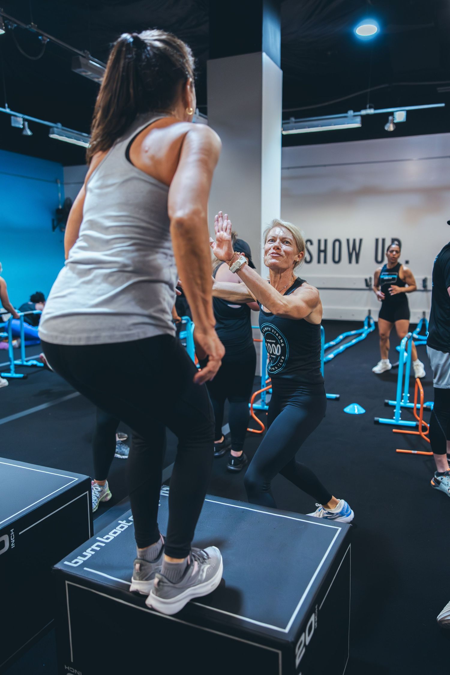 Fitness participants encouraging each other during platform exercises at a gym.