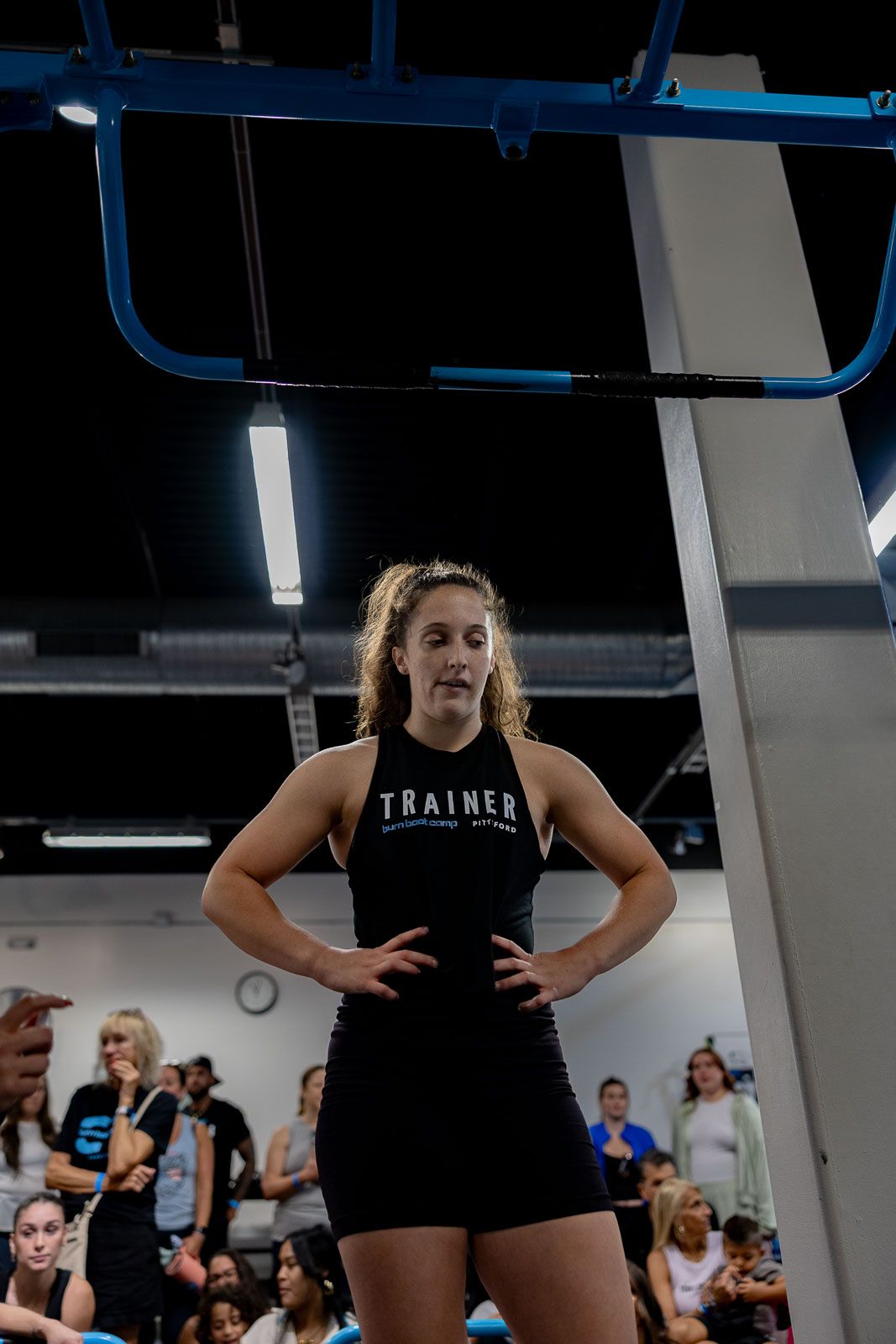 Fitness instructor in black athletic wear stands confidently in front of training equipment.