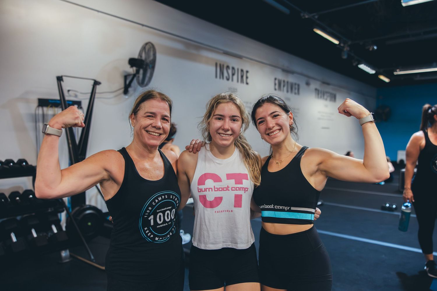 Three athletic women flexing their muscles and smiling at a fitness studio.