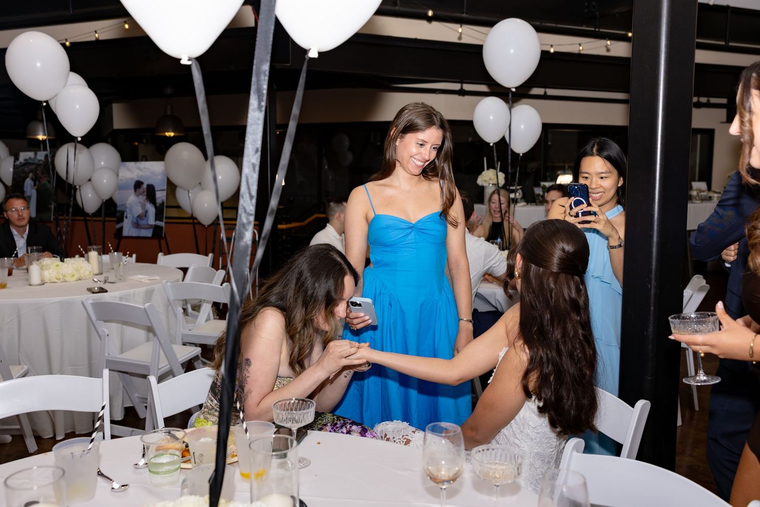 Wedding reception party guests dancing and celebrating together in an indoor venue decorated with white balloons.