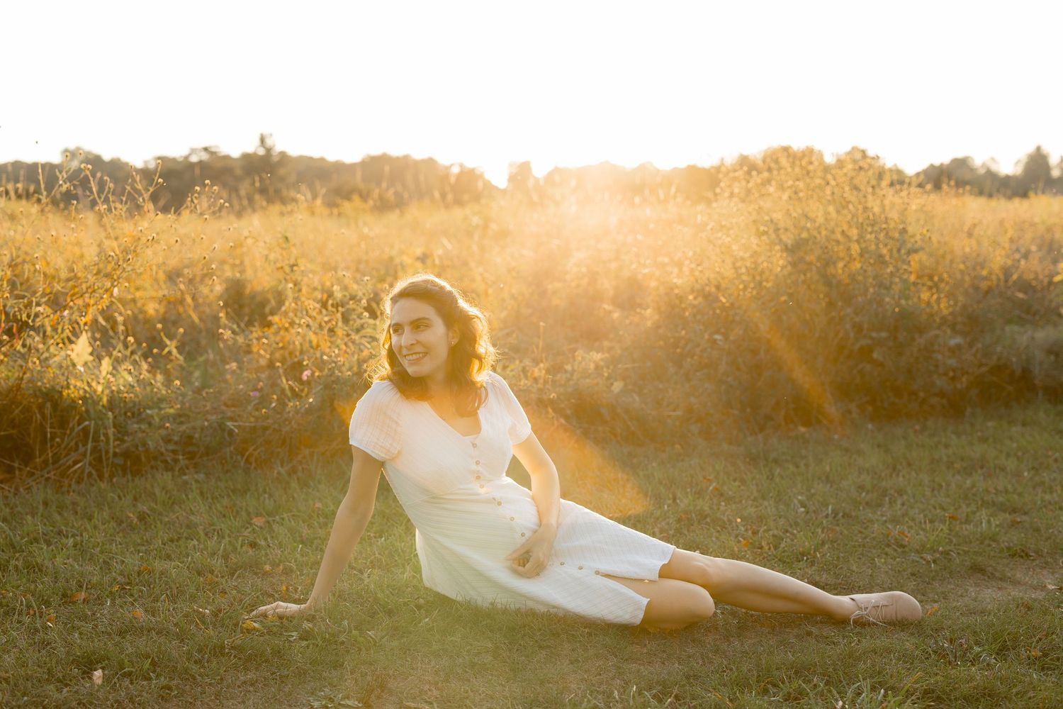 Person in white dress lying in golden field during sunset with warm glowing light creating dreamy atmosphere.