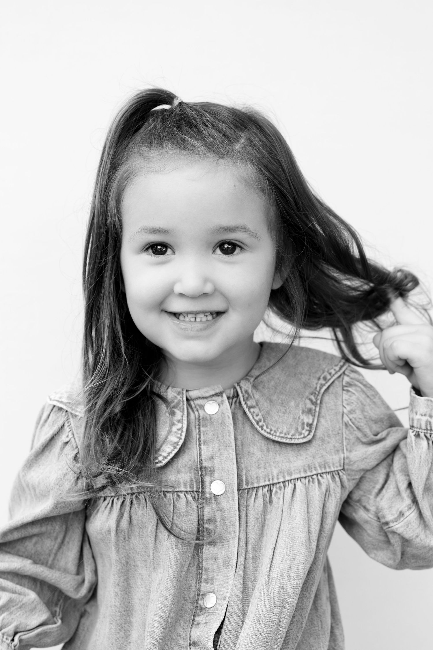 Black and white portrait series showing a young child in denim playfully posing and holding their hair.