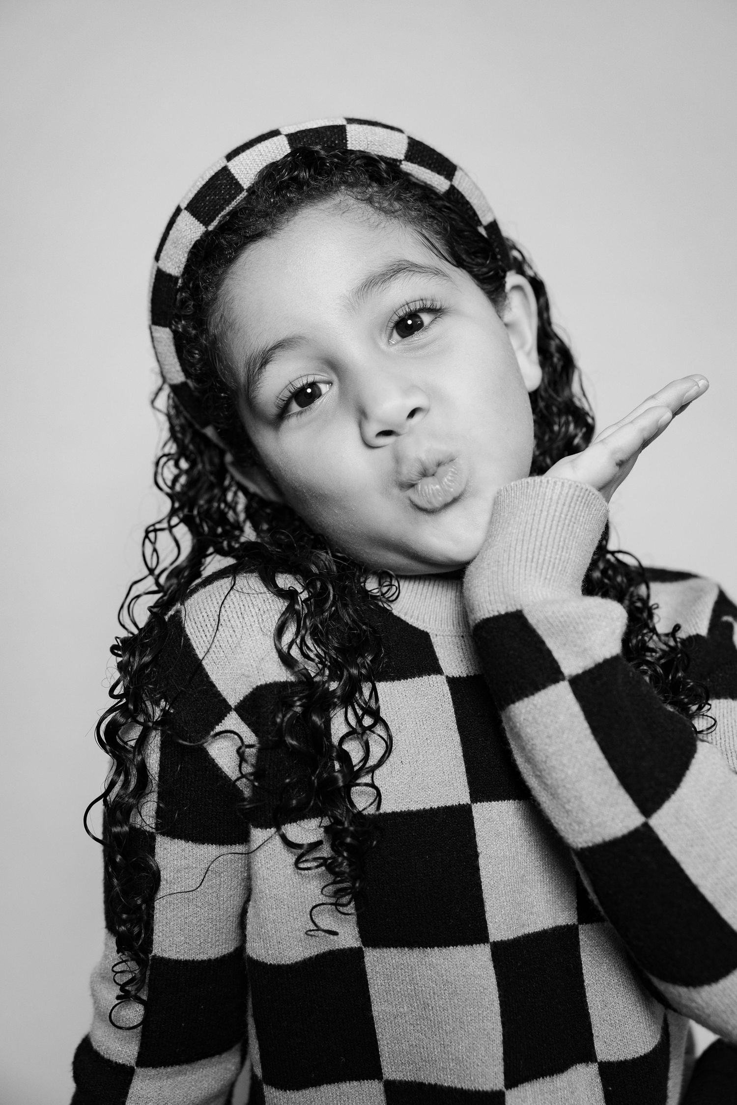 A series of black and white portraits showing someone in a checkered sweater making playful poses against a light background.