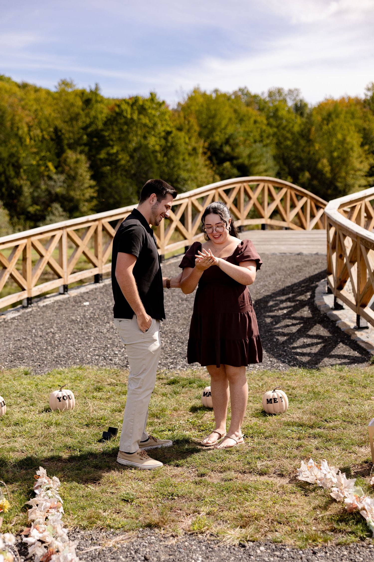 A couple shares a romantic moment on a wooden bridge surrounded by autumn foliage and fallen leaves.
