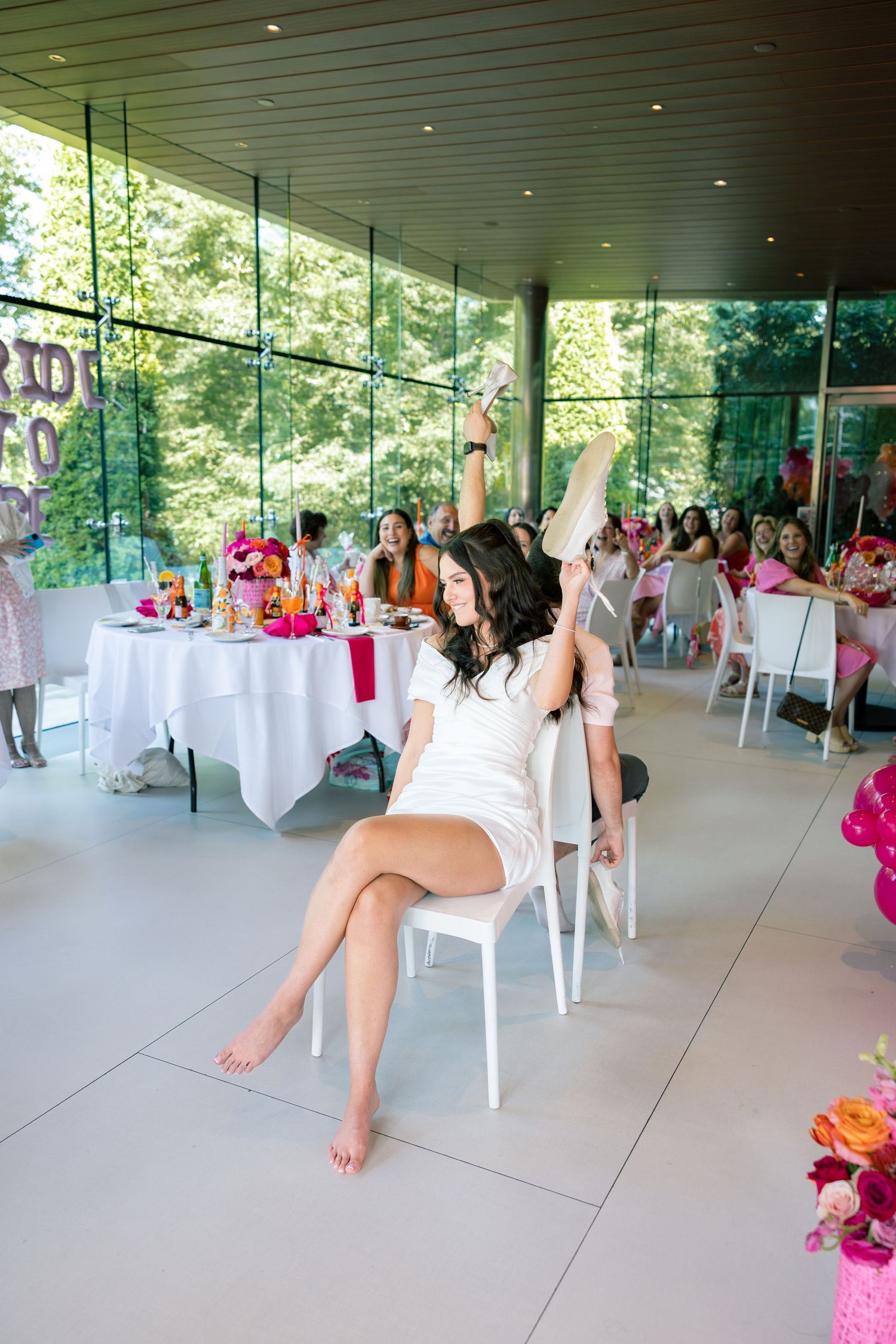 Elegant indoor-outdoor event space with white tables and chairs set up for a celebration with pink and floral accents.