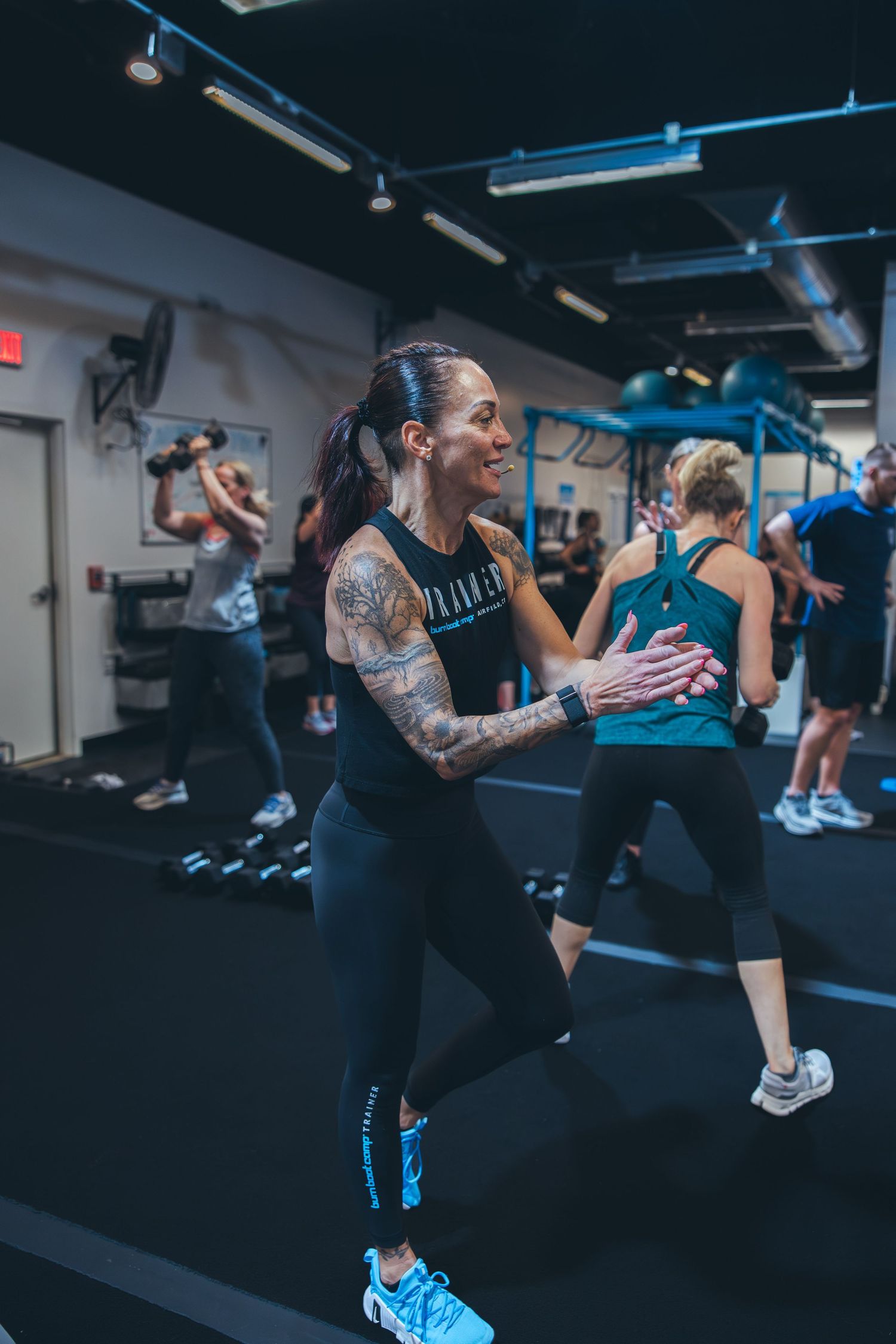 Fitness instructor leading a high-energy workout class in a modern gym with bright blue accents.