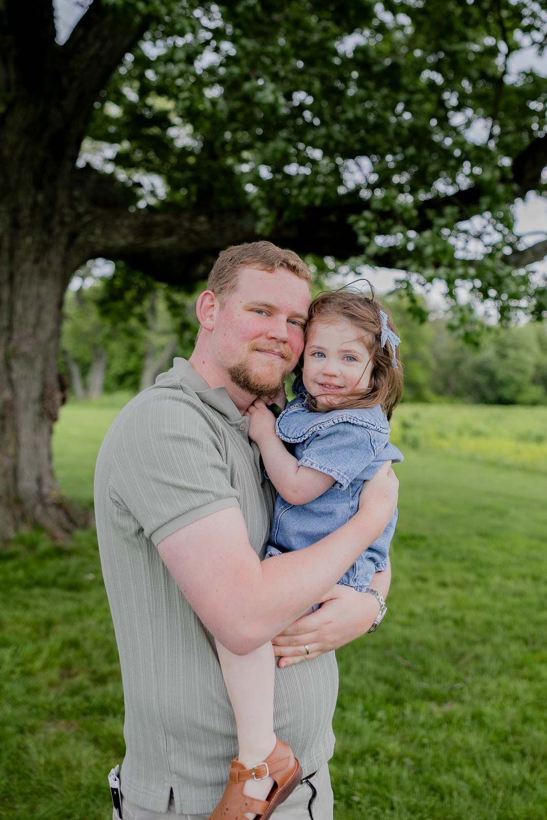 A tender outdoor portrait under a large tree in a lush green park setting.