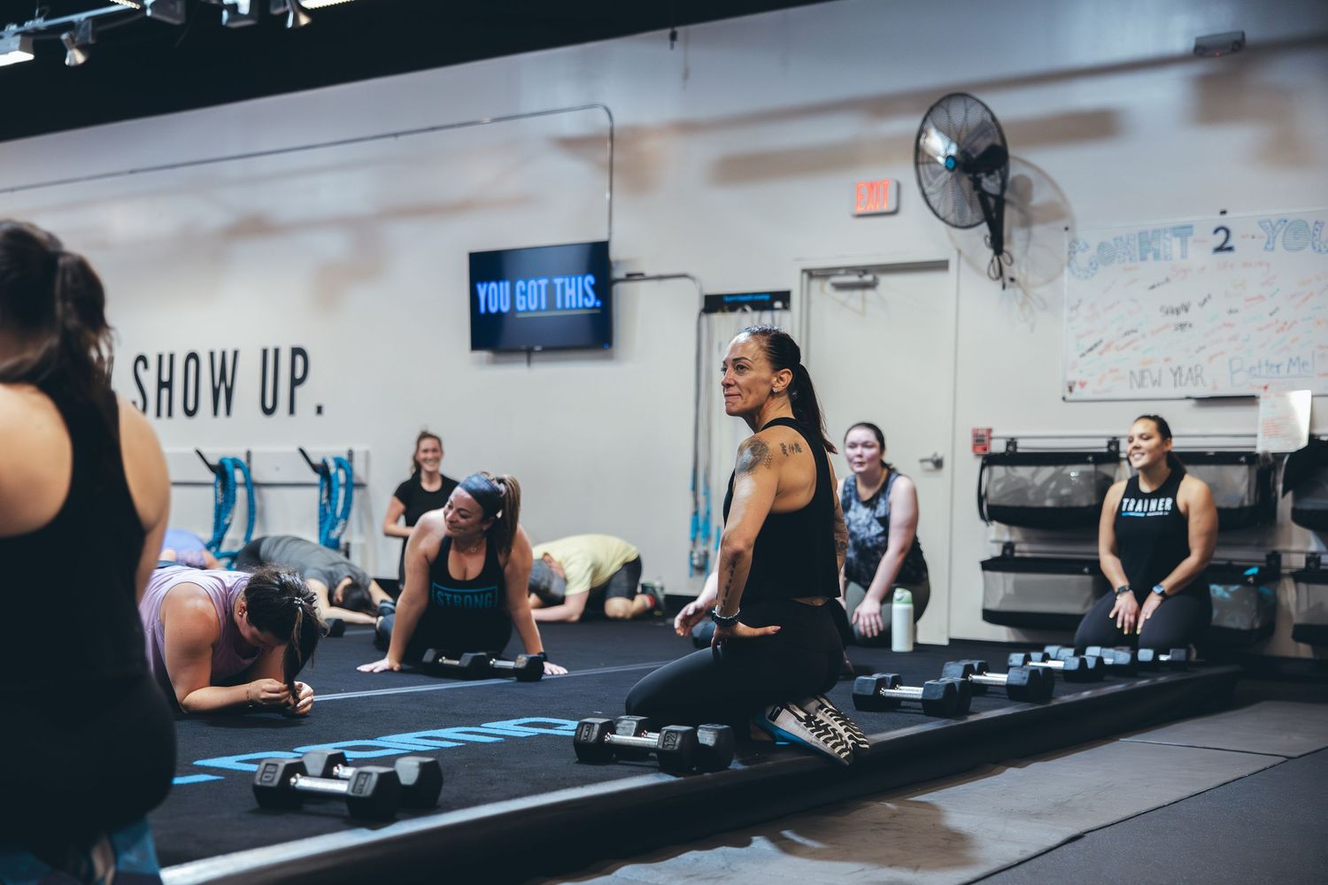 Fitness participants engaged in a floor workout session with motivational wall text in background.