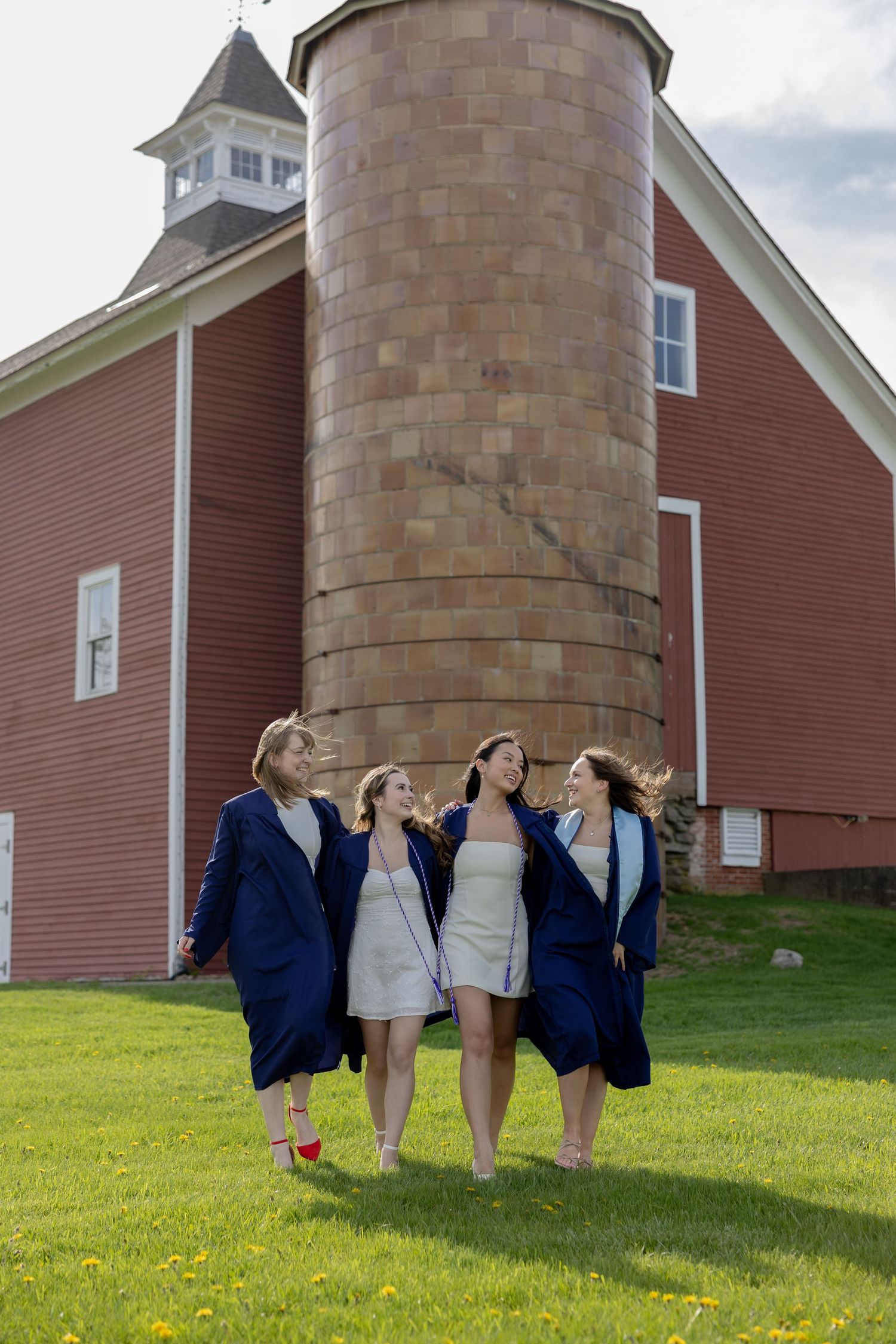 A group of graduates standing on grass next to a red barn with a silo on a sunny day.
