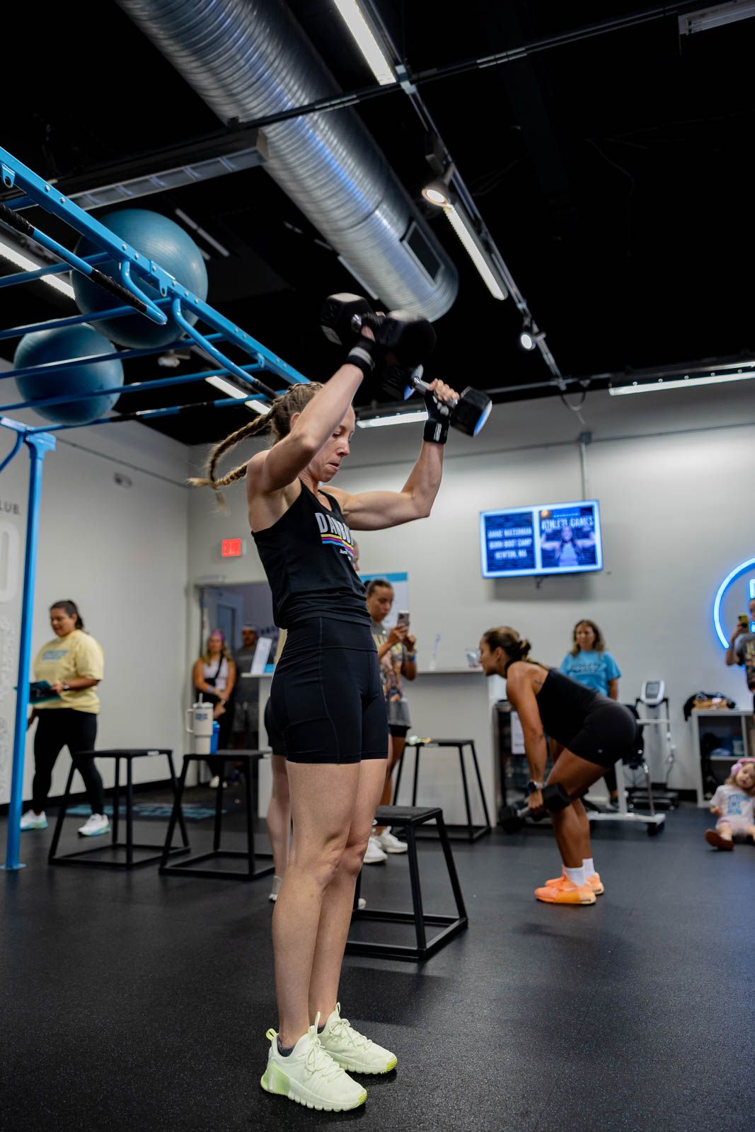 Person training on a pull-up bar at a modern fitness facility with exercise equipment visible in the background.