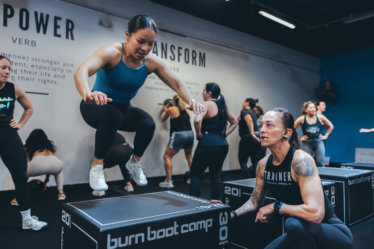 Athletes performing box jumps during high intensity workout at burn boot camp fitness studio.