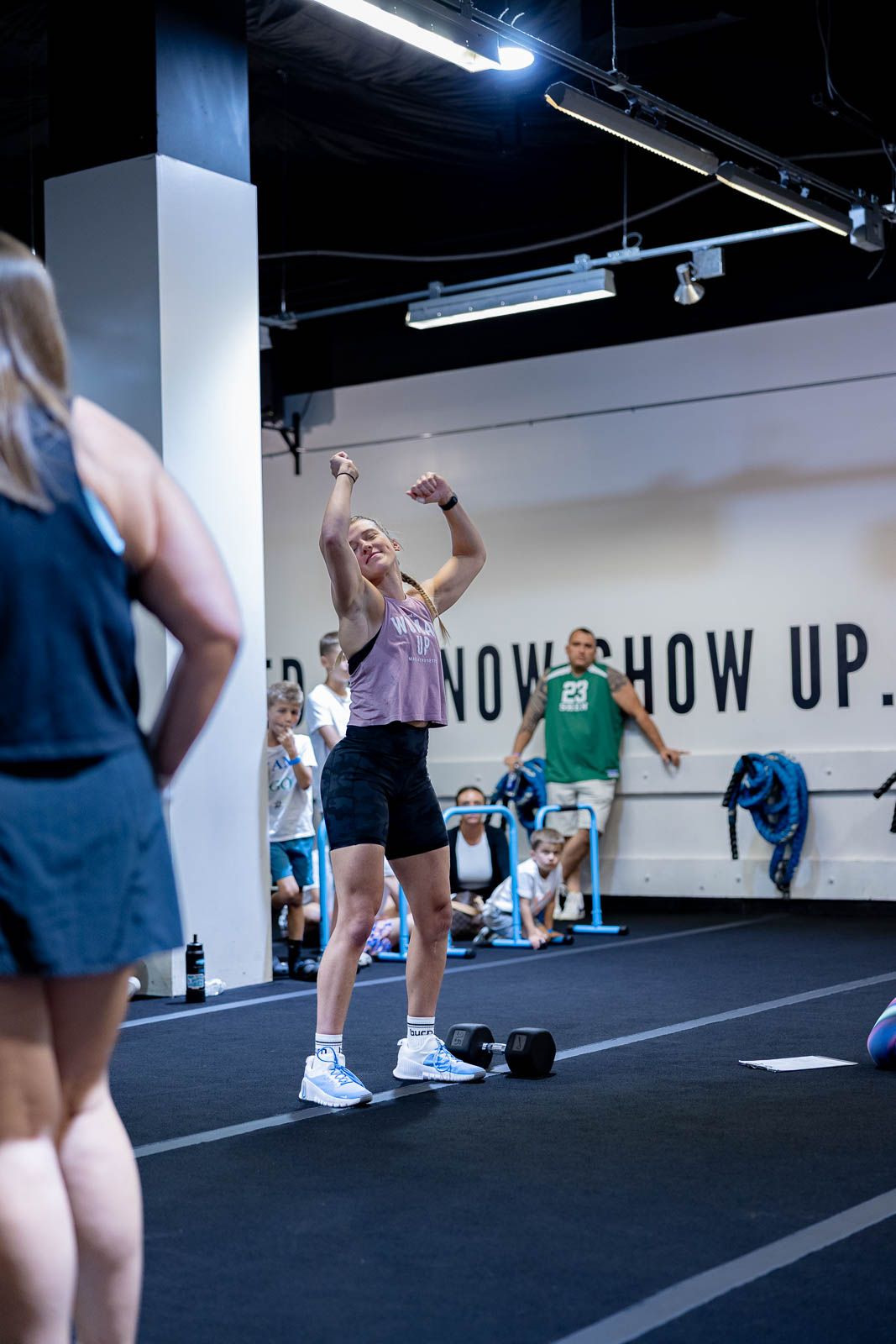 Athletes working out in a modern gym with 'SHOW UP' text visible on the wall during a high-intensity exercise class.