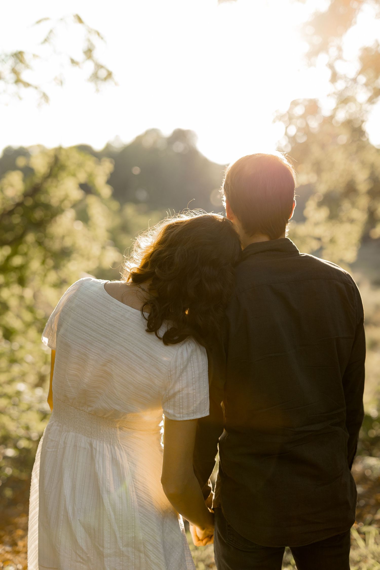 Couple walking together at sunset with golden sunlight filtering through trees in a romantic outdoor setting.