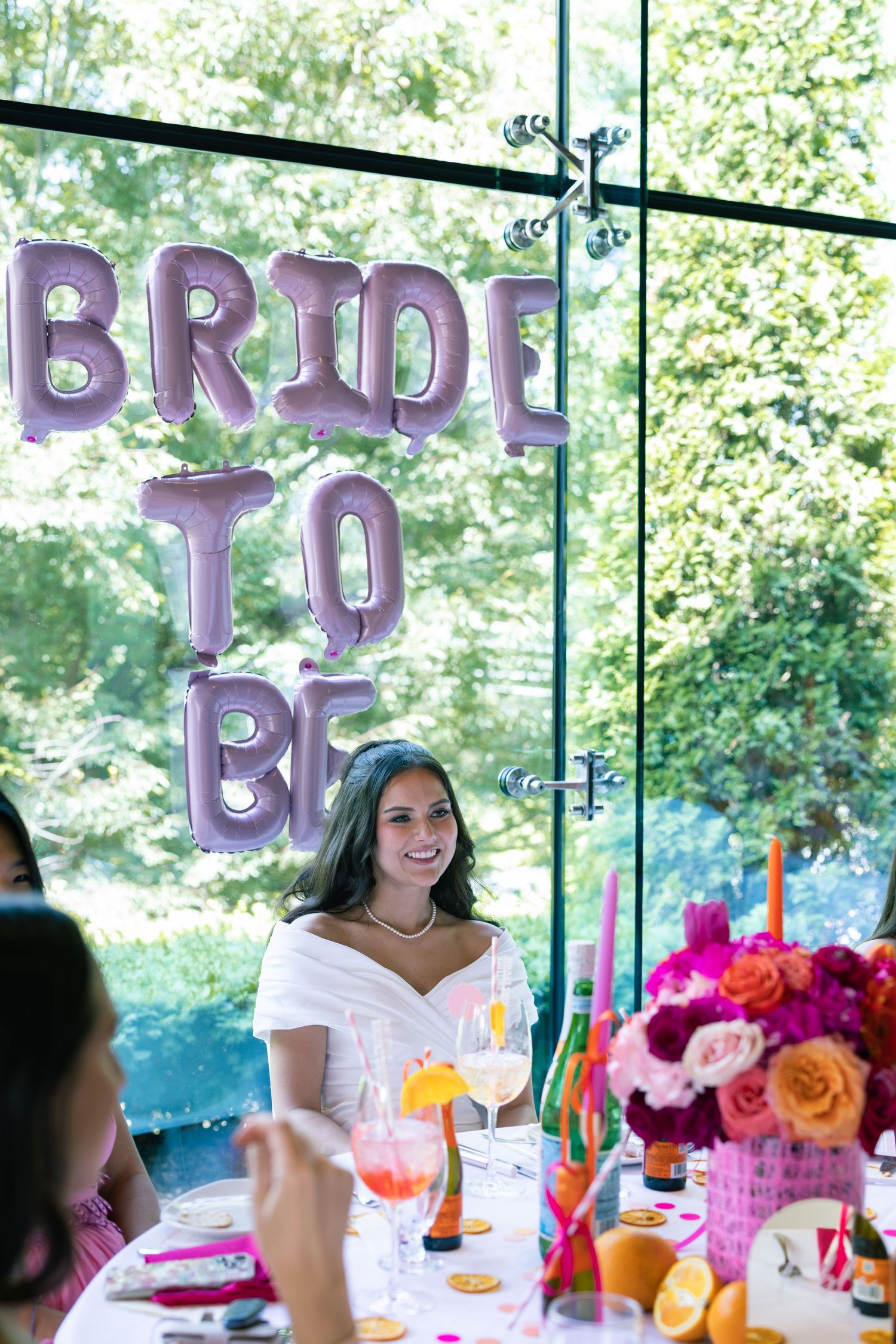 Bridal shower celebration with purple balloon letters spelling 'BRIDE TO BE' and colorful floral centerpiece on table.
