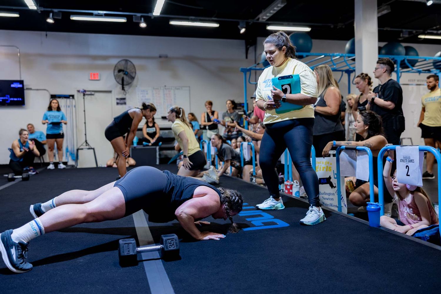 Athletes doing synchronized plank exercises in a spacious gym while others observe from the sidelines.