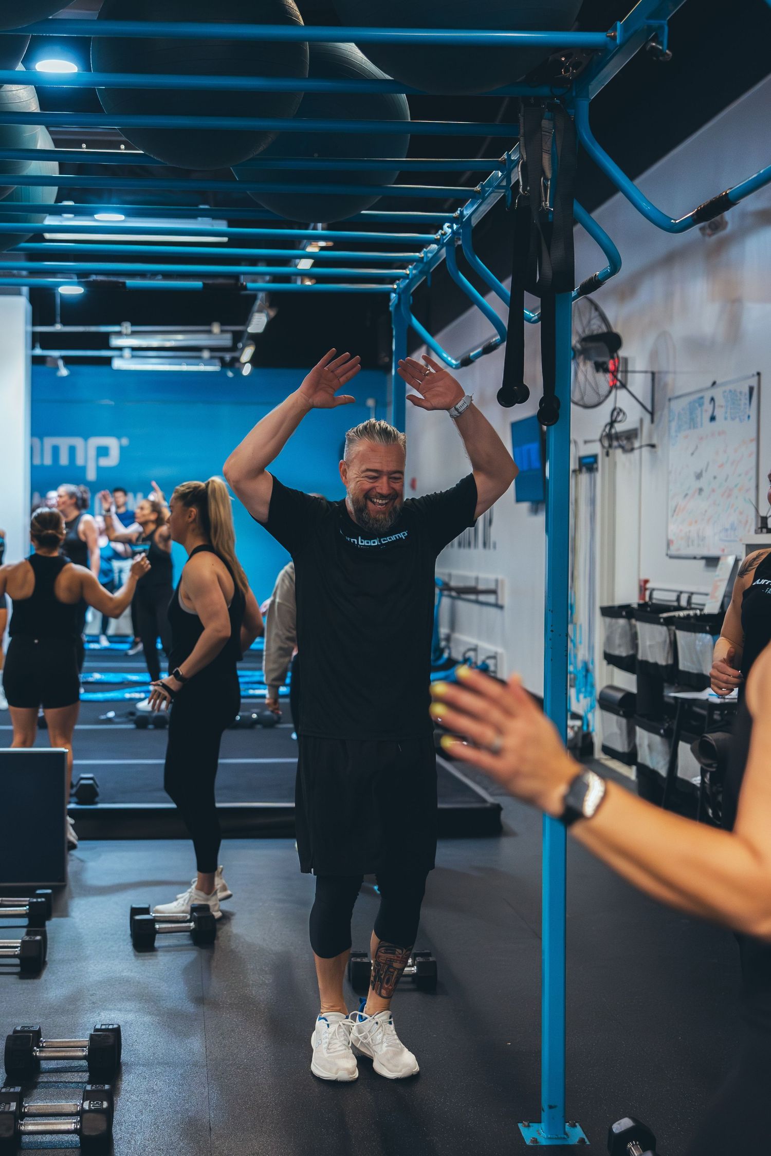 Person in black athletic wear jumping with raised arms during an energetic workout class at a fitness studio.
