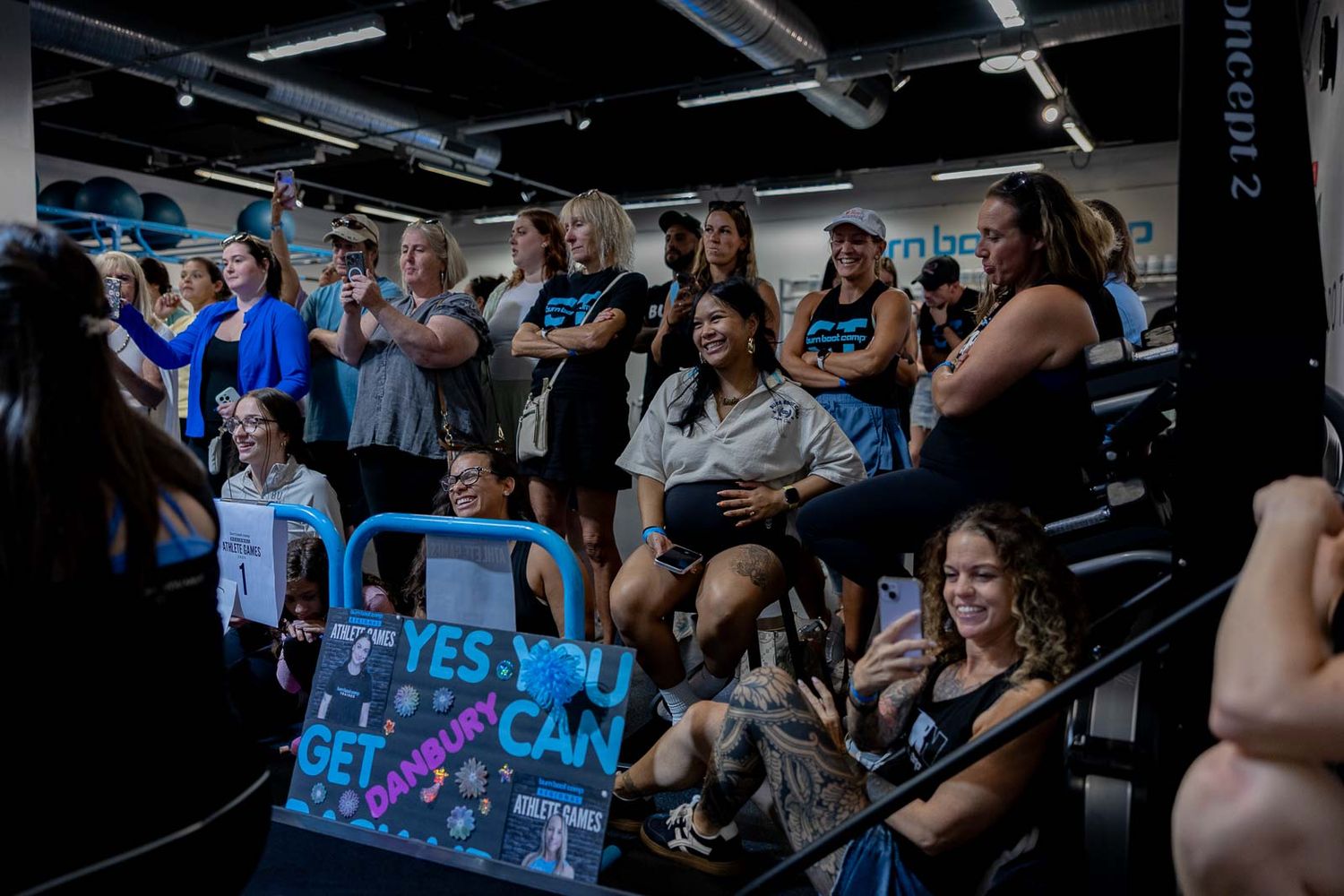 A group of spectators watching and cheering during a fitness competition in an indoor gym setting.