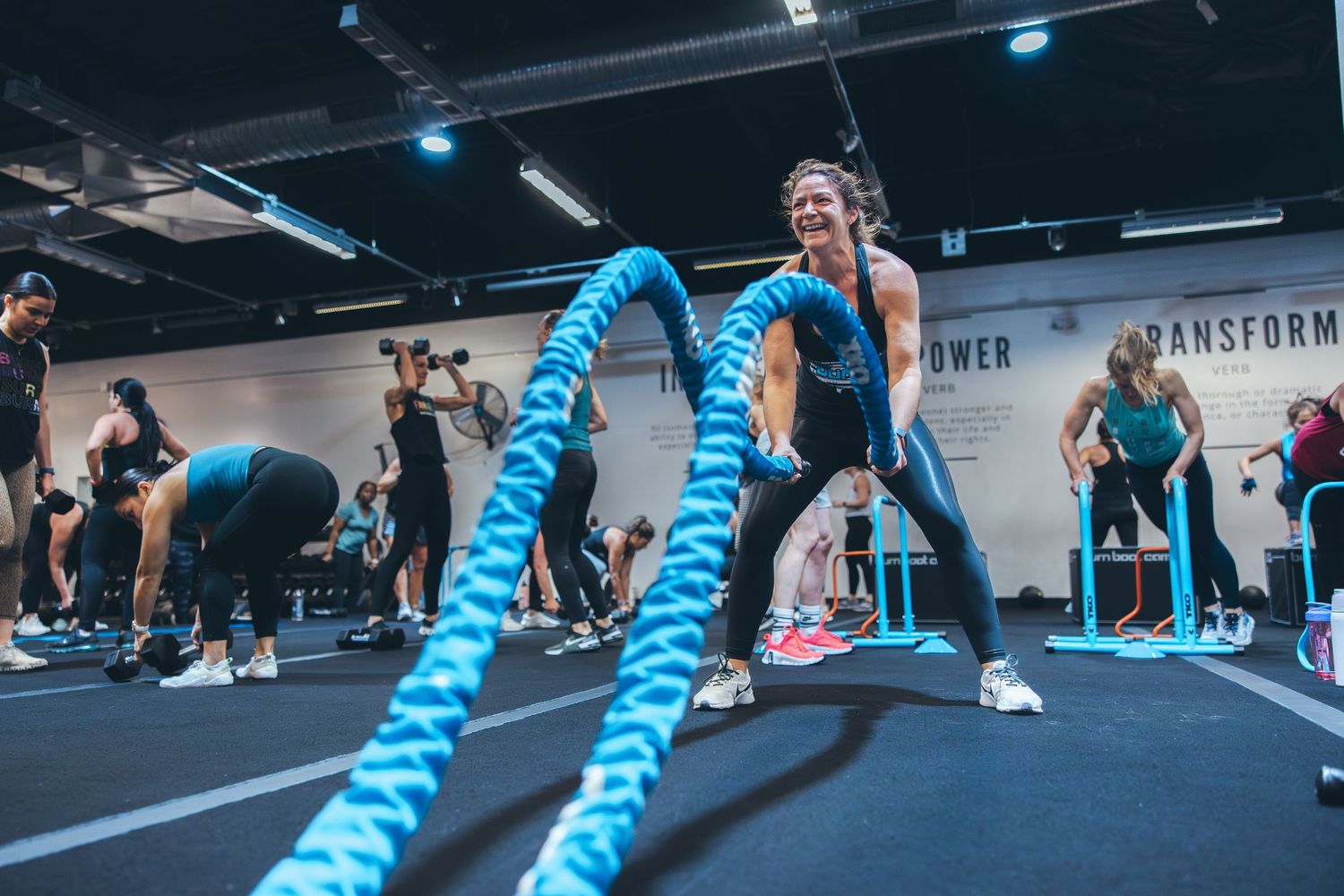 Athletes perform battle rope exercises during a high-intensity workout class in a fitness studio.