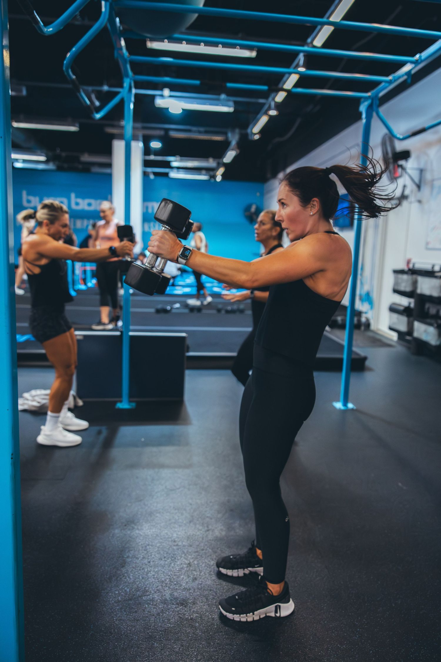 Athletes perform kettlebell swings during an intense workout session in a modern gym with blue accents.
