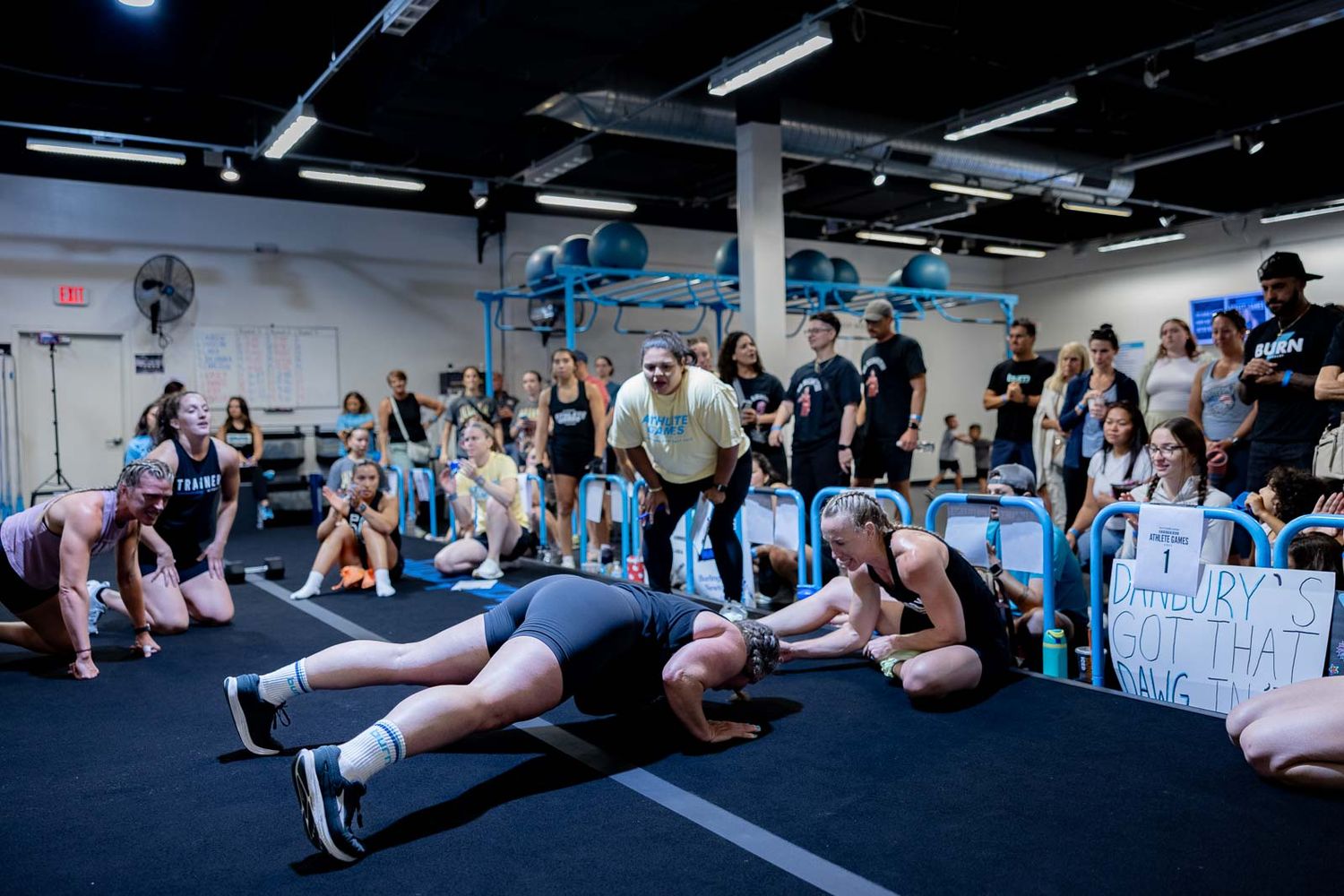 Fitness enthusiasts performing planks and core exercises on a dark gym floor during a group workout.
