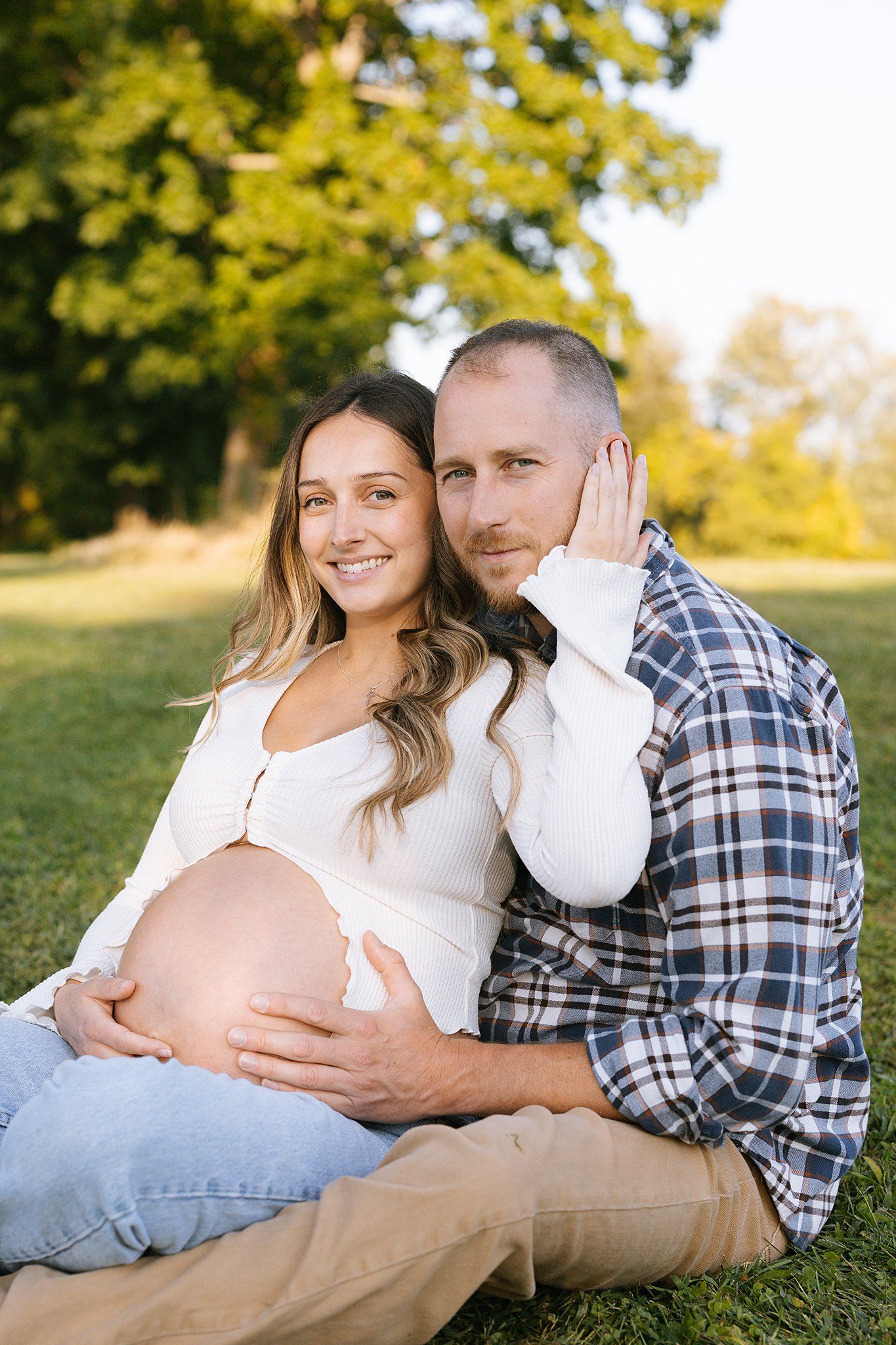 Expecting couple poses together on grass during sunset maternity photoshoot.