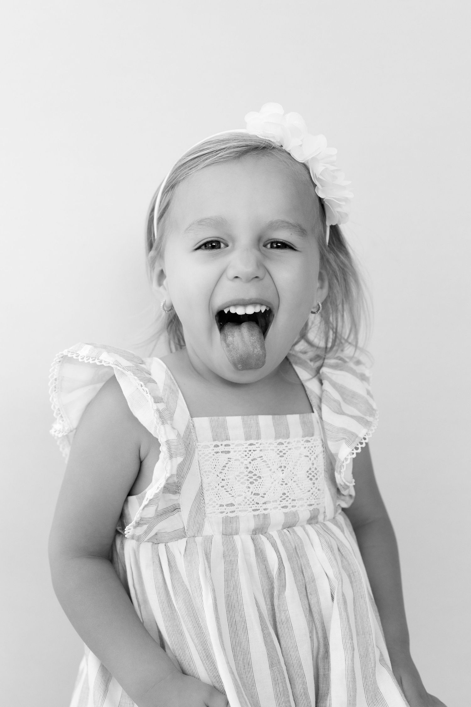 Black and white photo series showing a child in a white lace dress making silly expressions and sticking out their tongue.