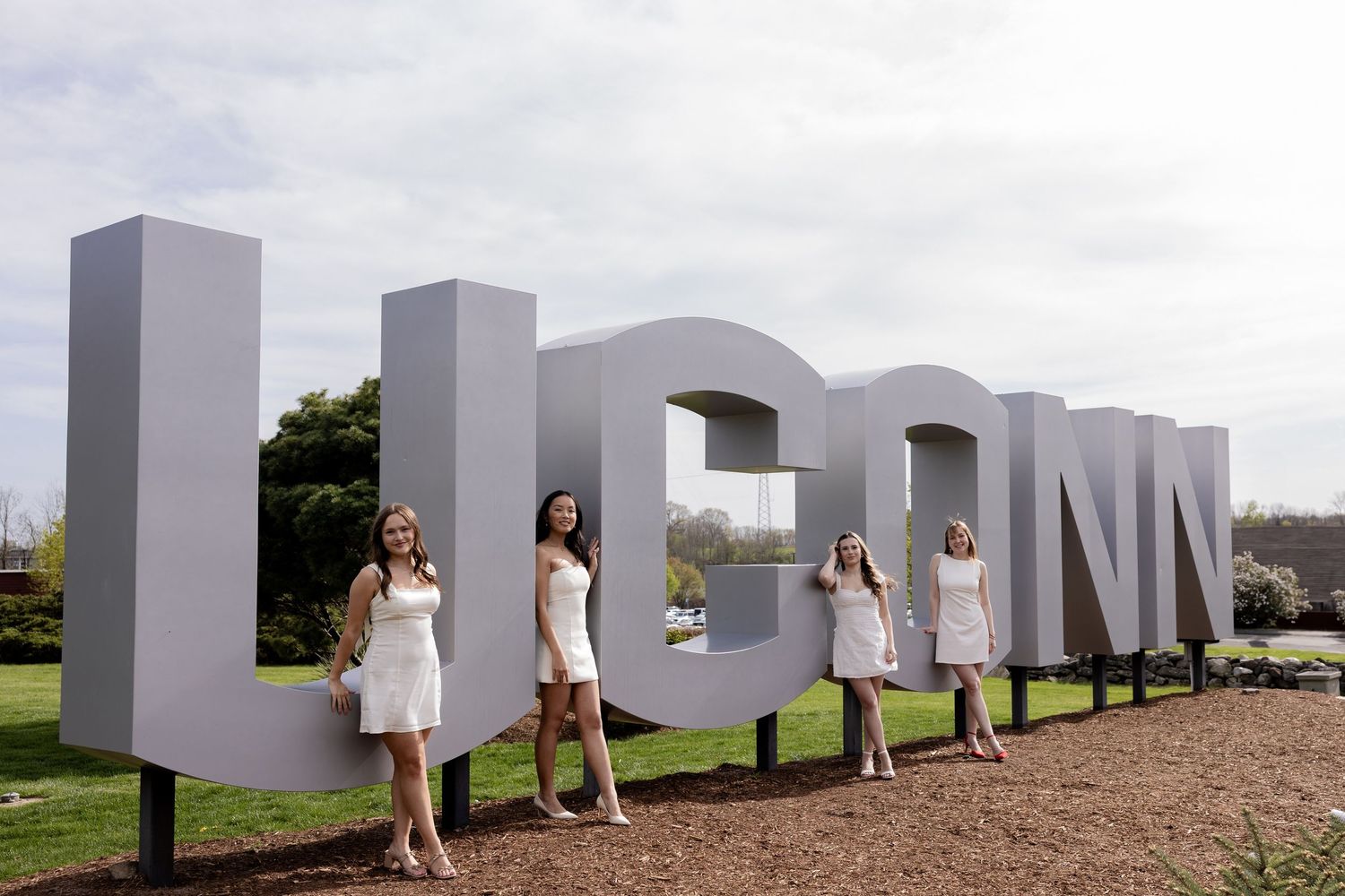 Five people pose in front of large white UCONN letters on a sunny day.