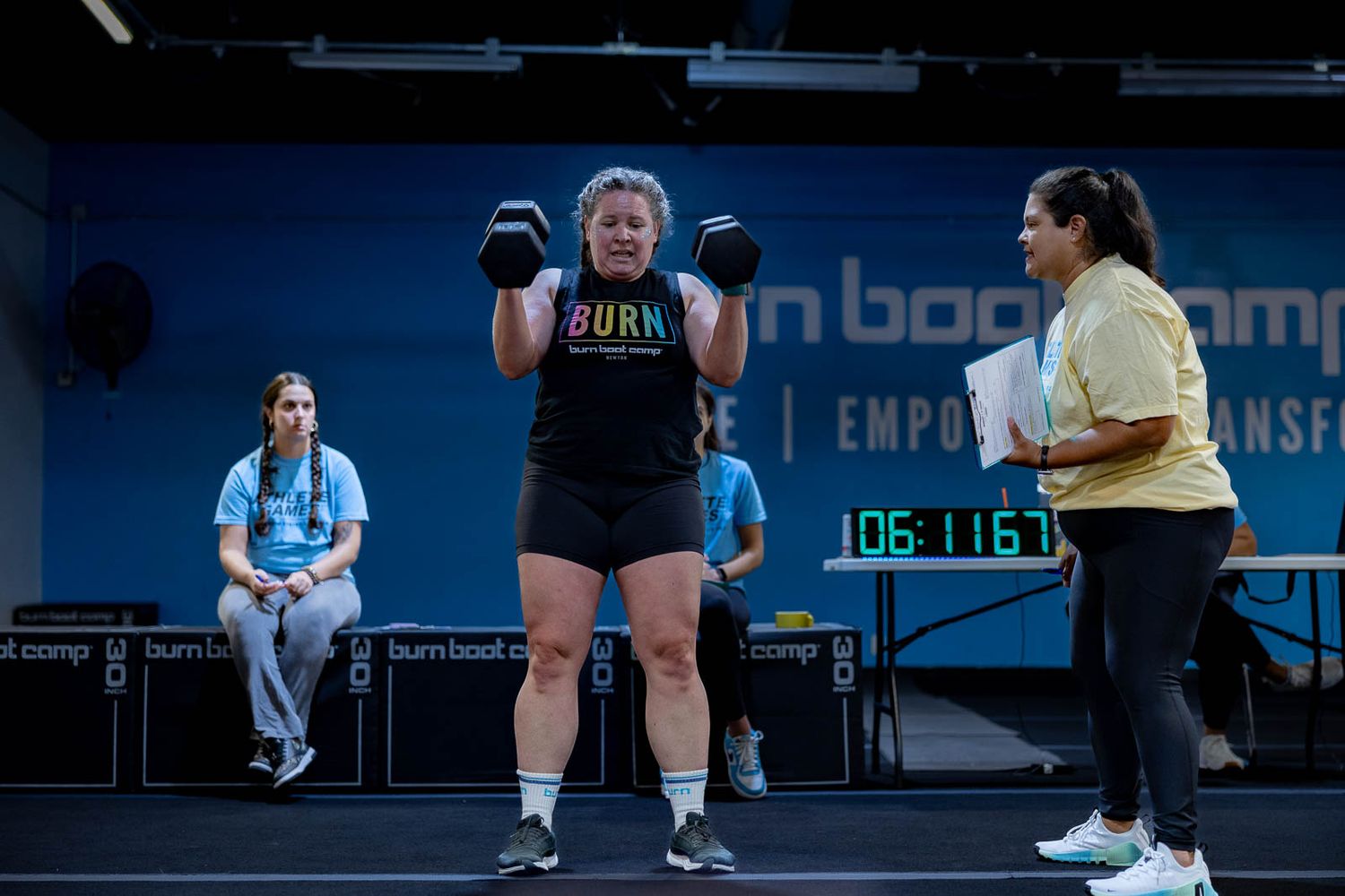 Athletes performing burpee exercises during an intense workout class at a blue-lit fitness gym.