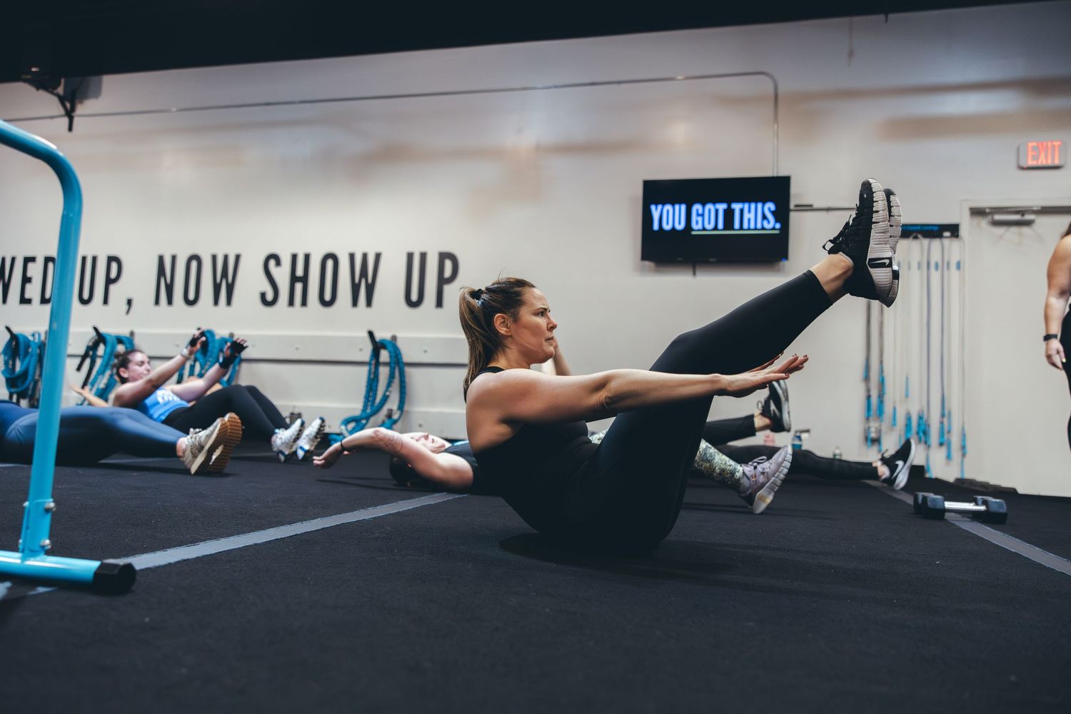 Person demonstrating perfect form during a V-sit core exercise on a gym floor.