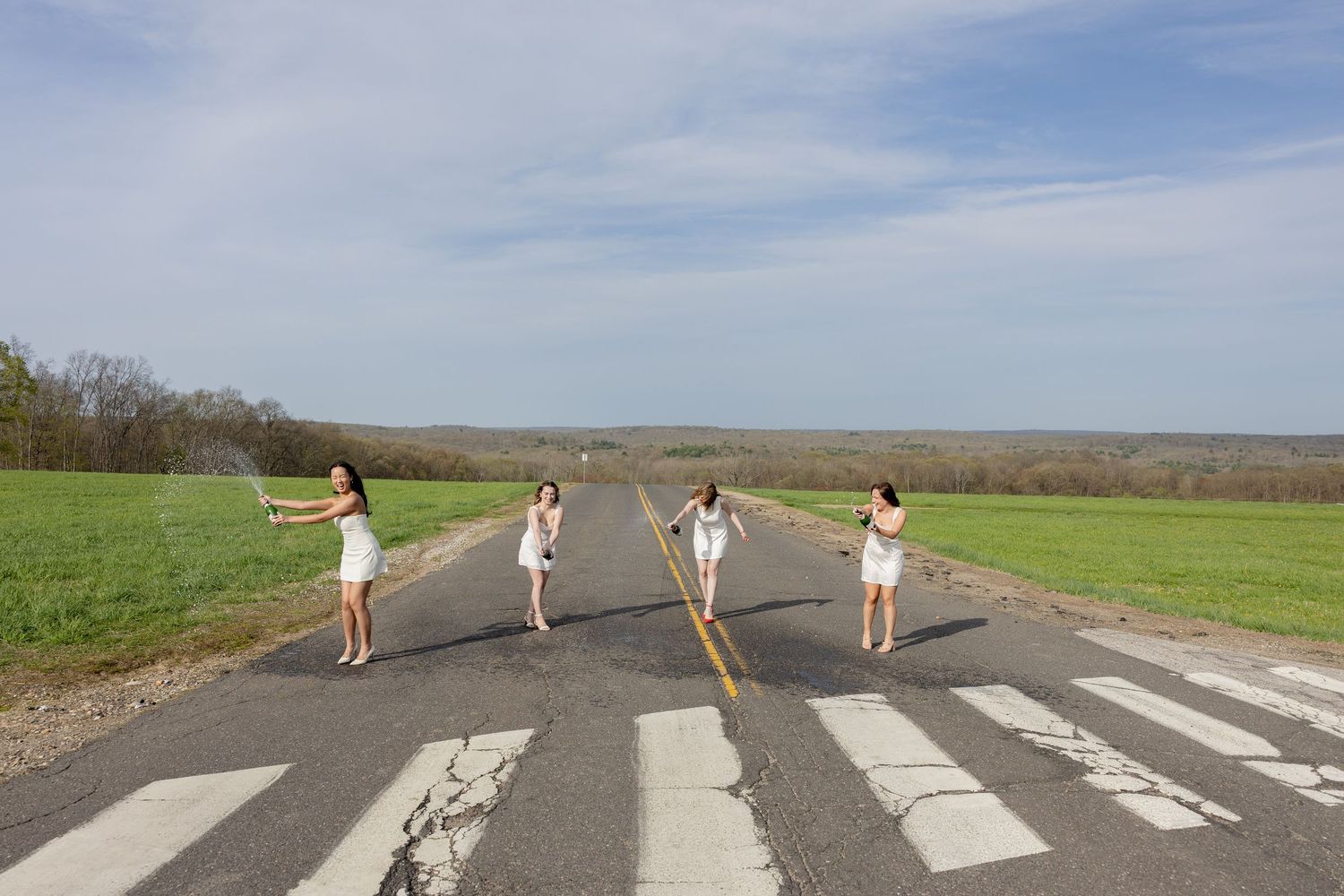 People recreate the iconic Abbey Road album cover pose on an empty rural road on a sunny day.