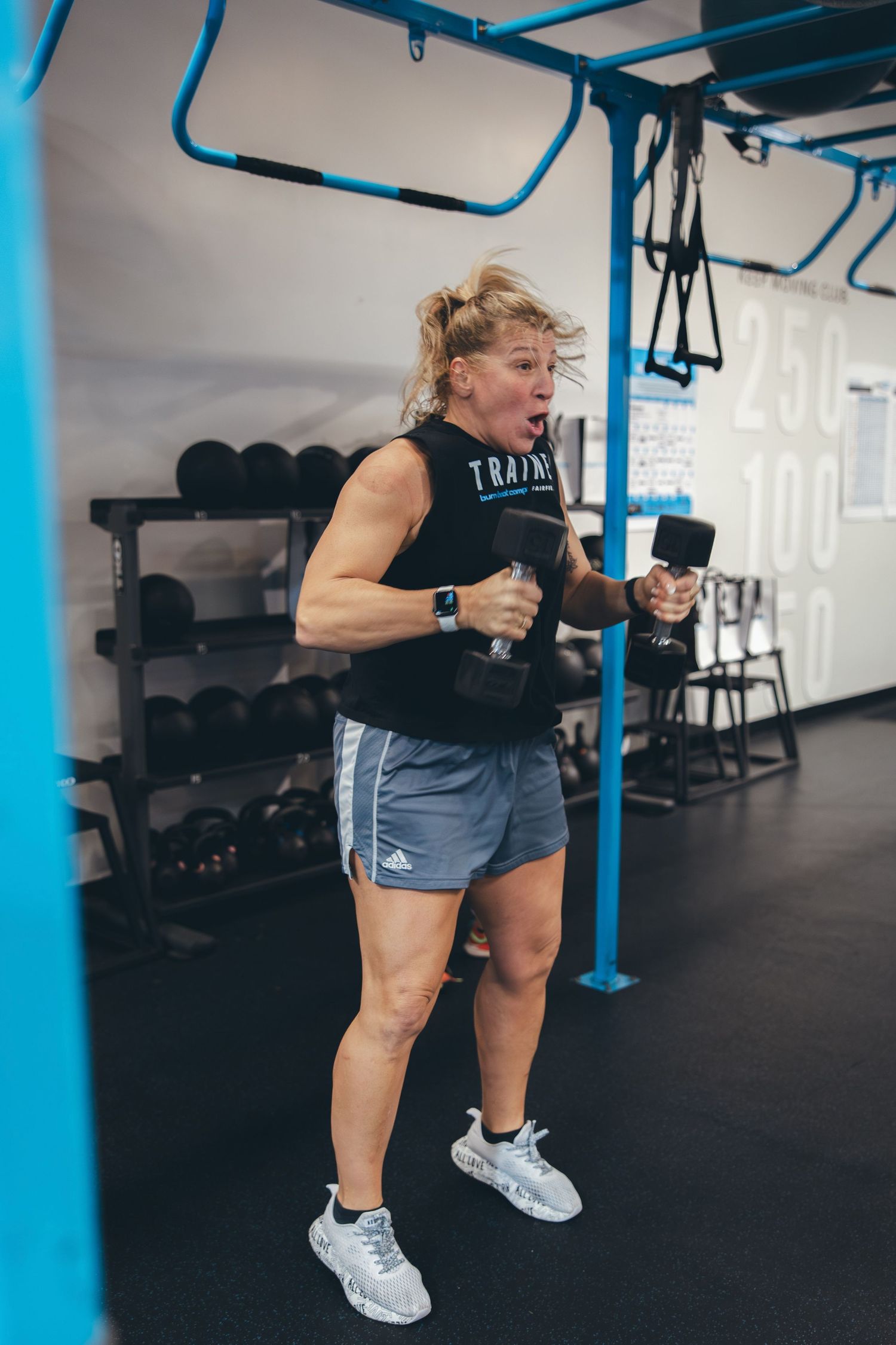 Athletic person exercising with dumbbells in modern gym facility with blue overhead equipment.
