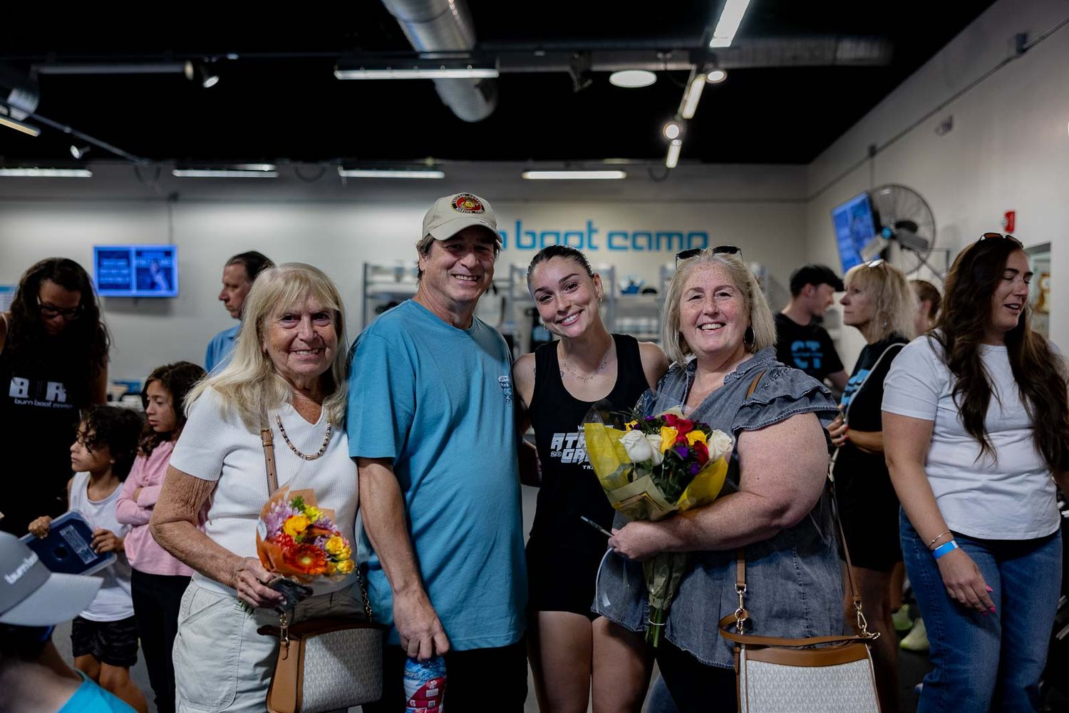 Group of people gathered at a boot camp fitness center holding colorful floral bouquets.