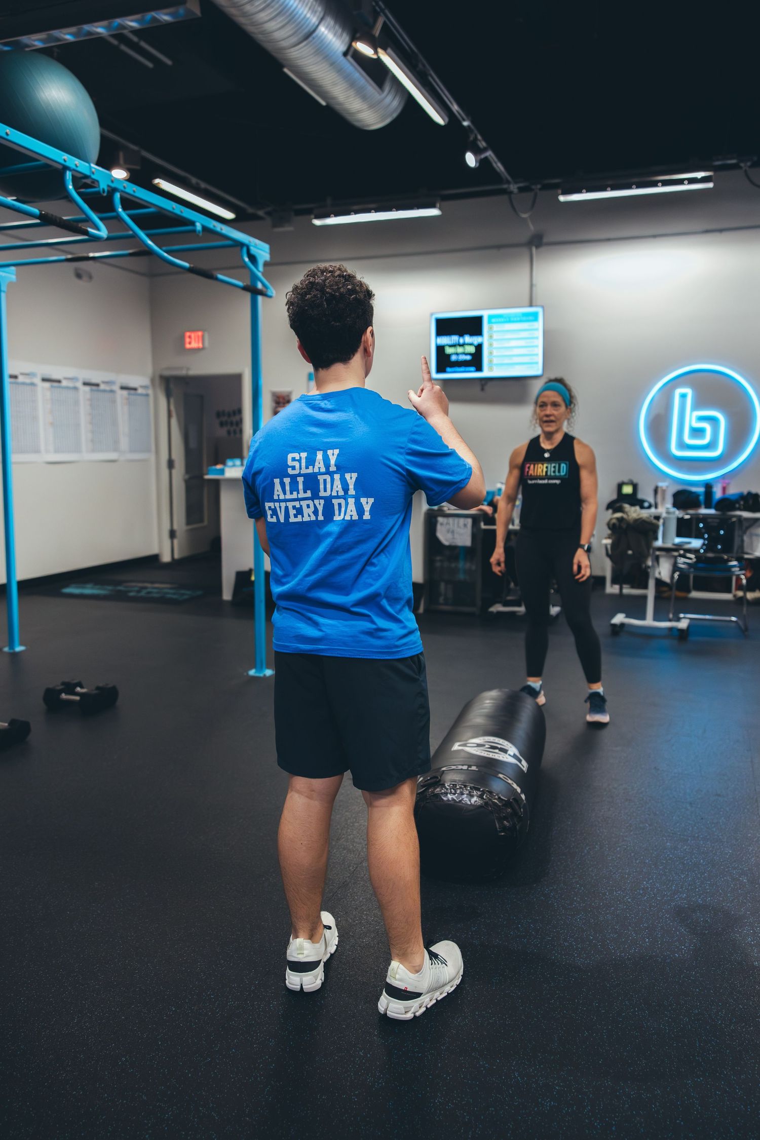 Person in blue shirt reading 'Slay All Day Every Day' stands in modern gym facility.
