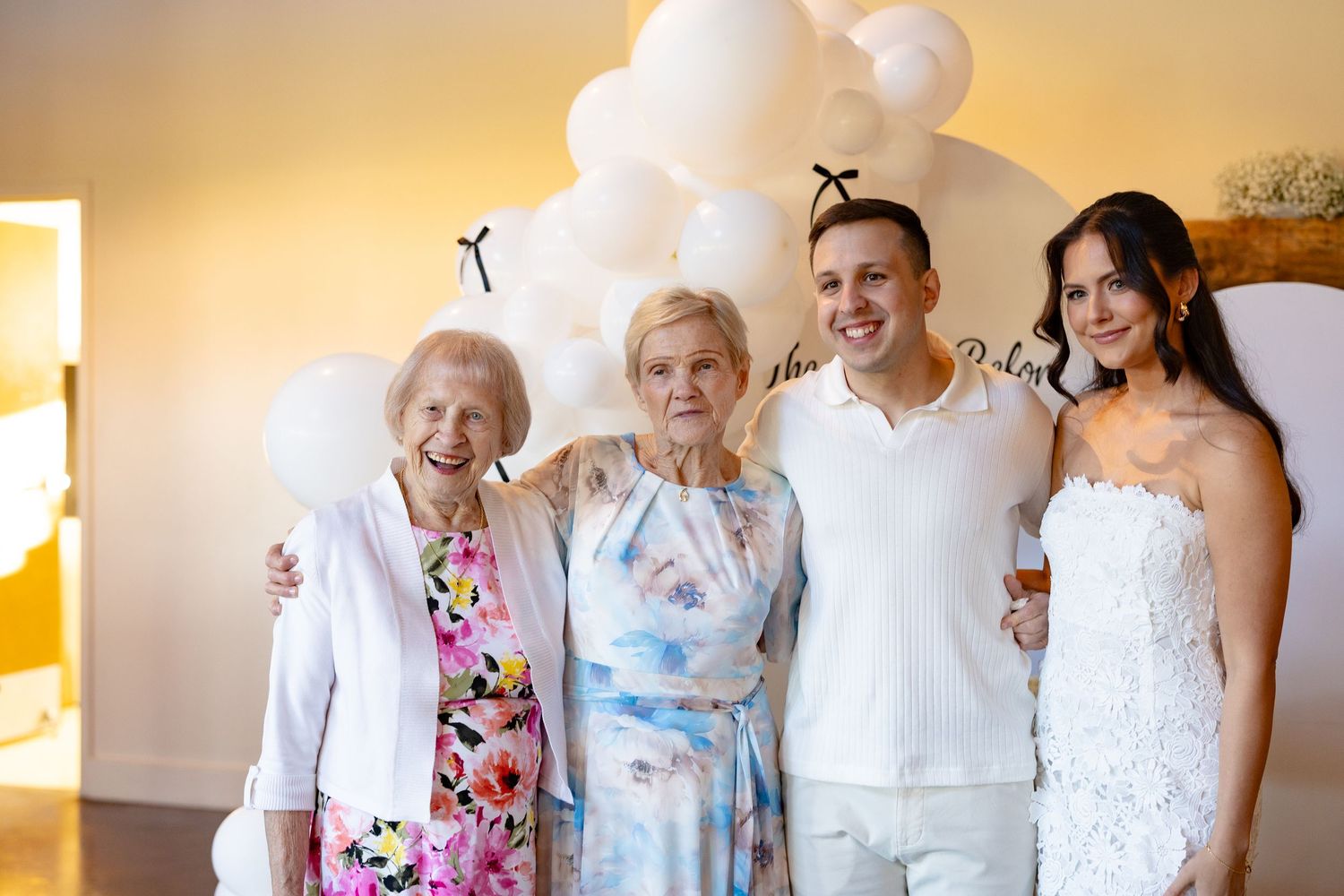 Group photo of wedding guests in light colored attire posing together outdoors.