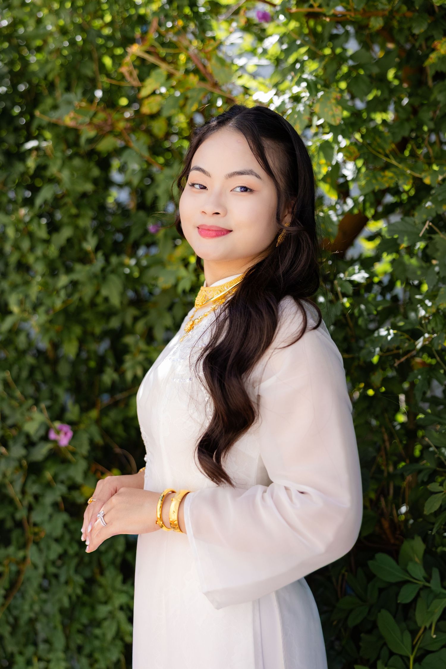 A person in a white sweater poses outdoors against a green leafy background in a photo series.