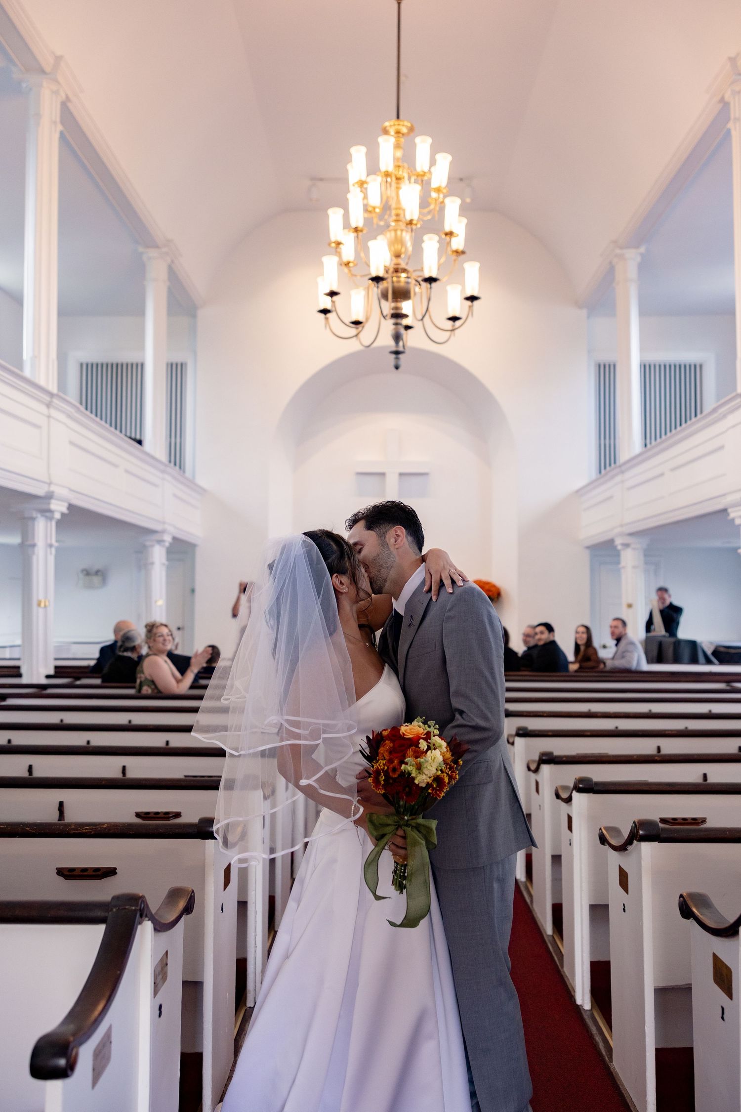 A sequence of wedding photos showing a couple sharing their first kiss in a bright white church sanctuary.