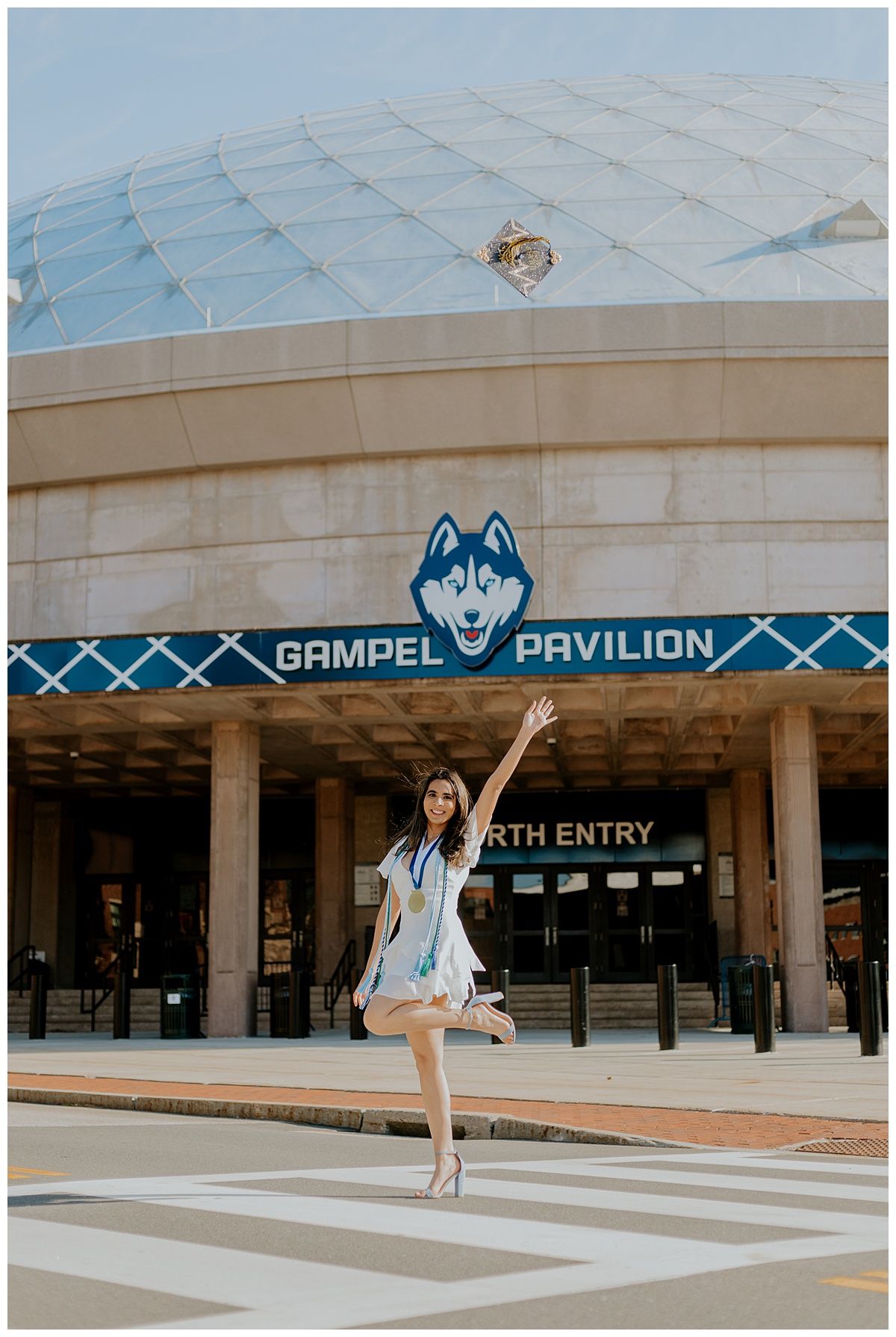 Graduate strikes a pose in front of the Gampel Pavilion at UConn during commencement.