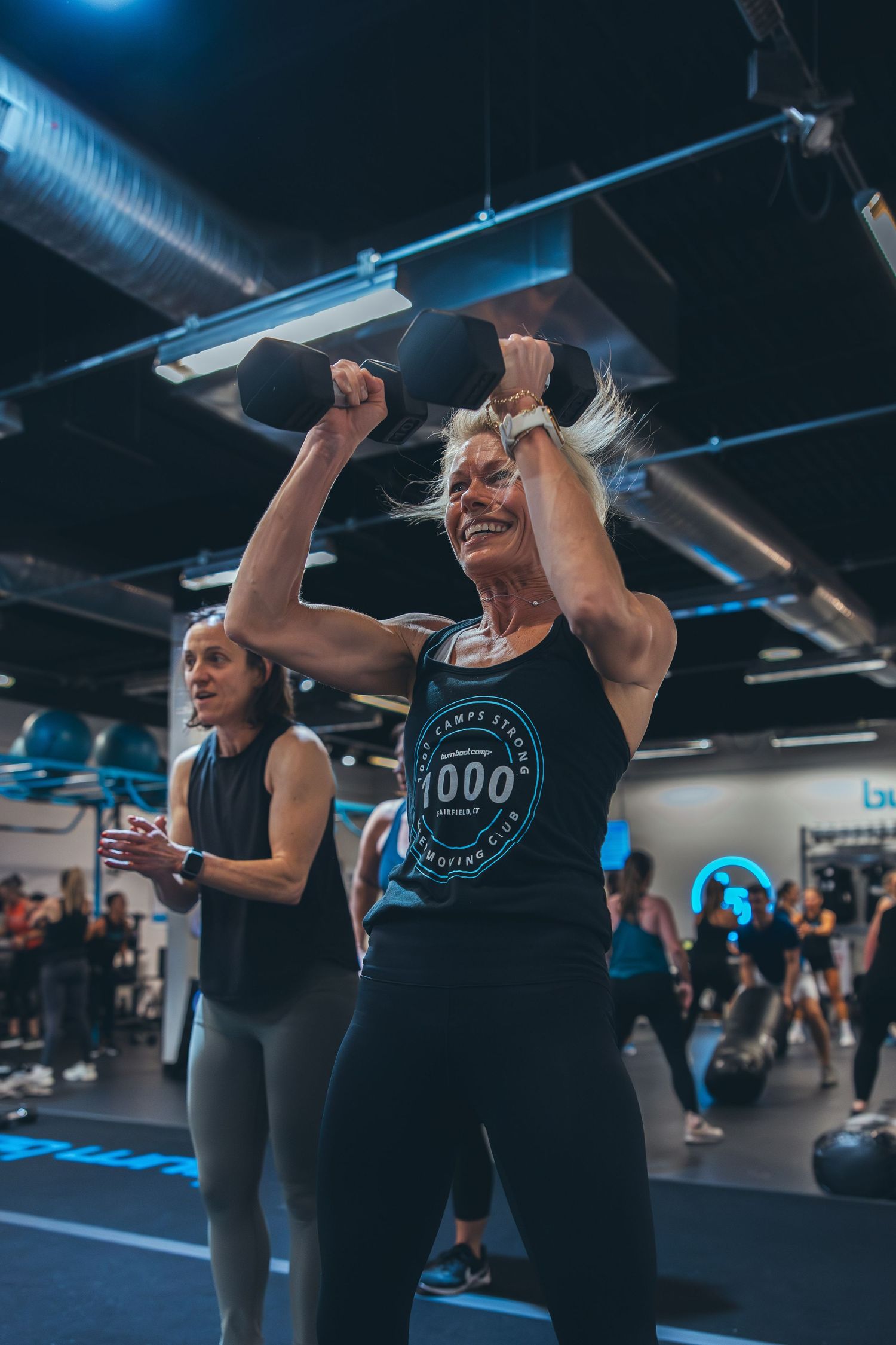 Fitness enthusiasts celebrate during a high-energy workout class with blue lighting and industrial decor.