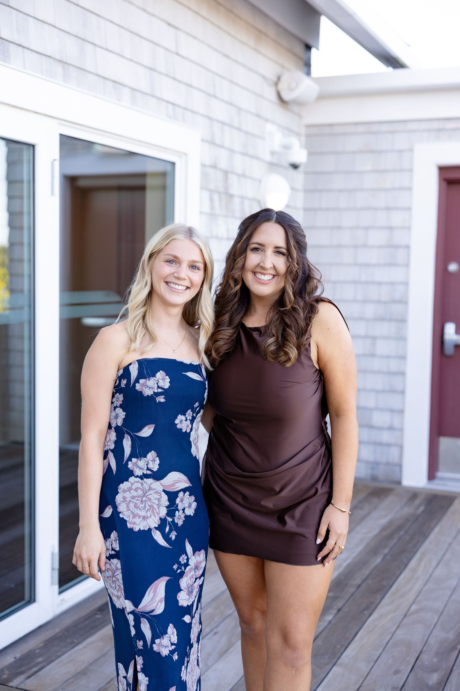 Friends pose together on wooden deck outside white building with glass windows.