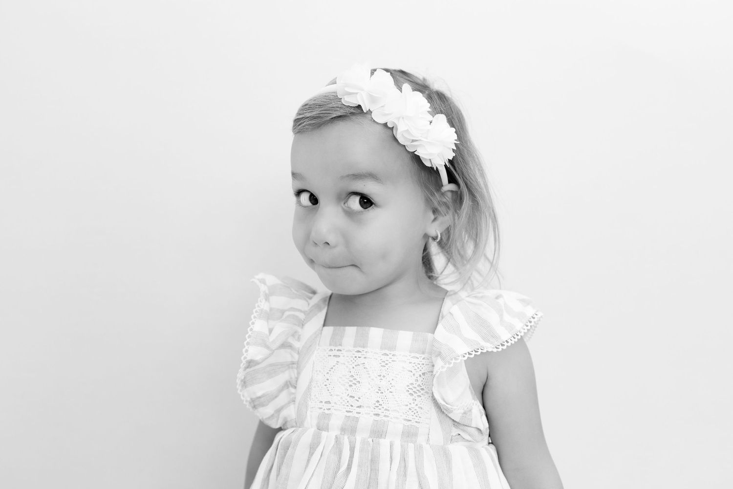Black and white portrait of a young child wearing a white dress with ruffled sleeves and floral headband.