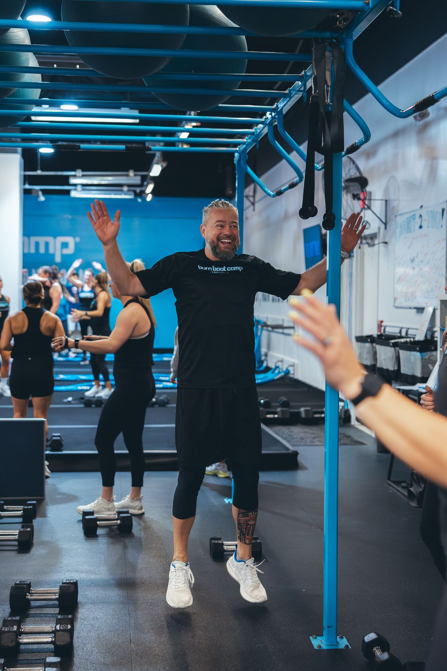 Energetic trainer leading a group fitness class with raised arms while participants follow along.