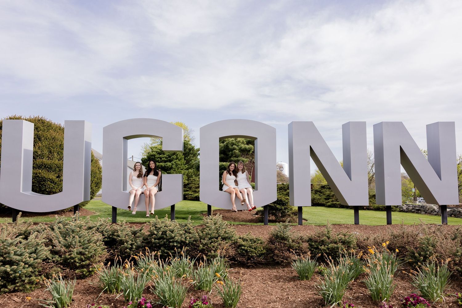 Large white UCONN letters form a photo backdrop display surrounded by landscaping on a cloudy day.