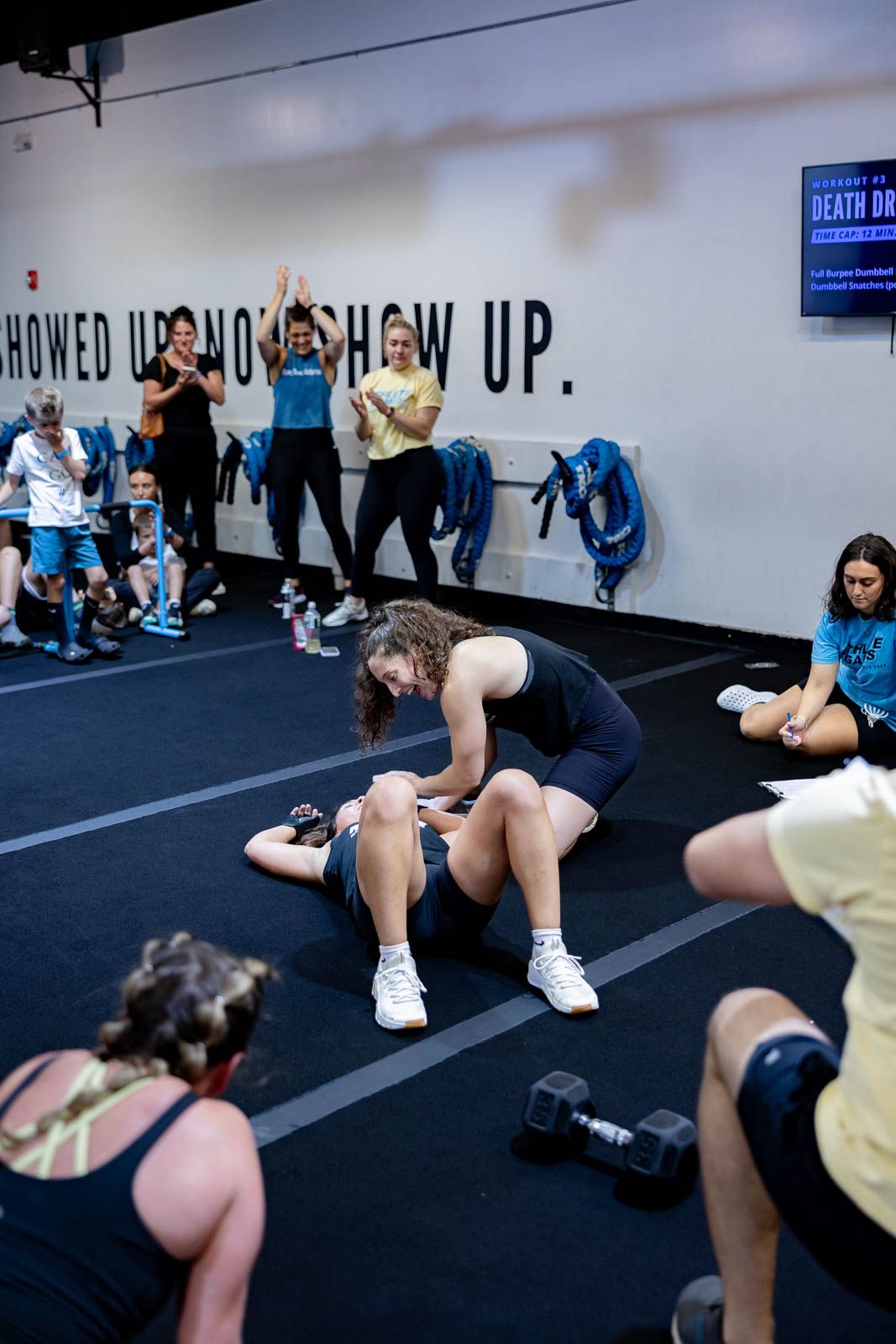 Athletes perform stretching exercises on blue mats during a group fitness class in a gym.