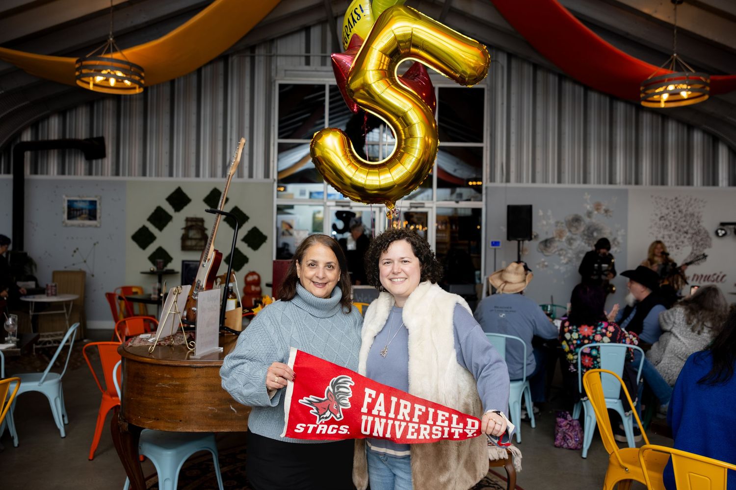People gather at an indoor party or celebration with festive decorations and lighting.