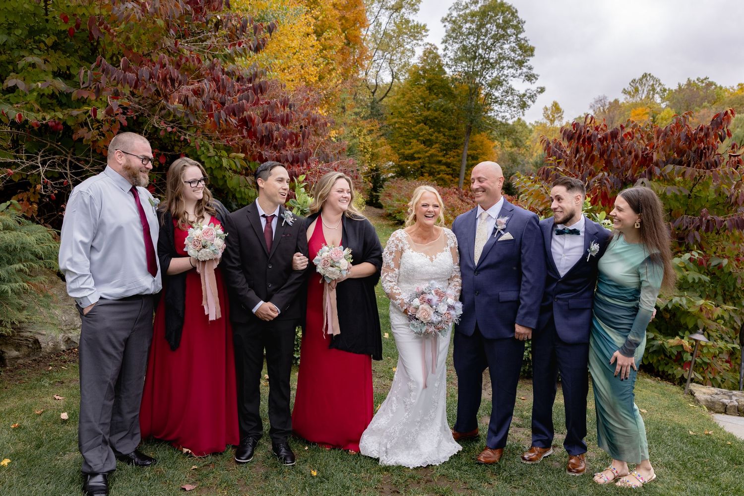 Wedding party poses outdoors in autumn with vibrant red and orange fall foliage in the background.
