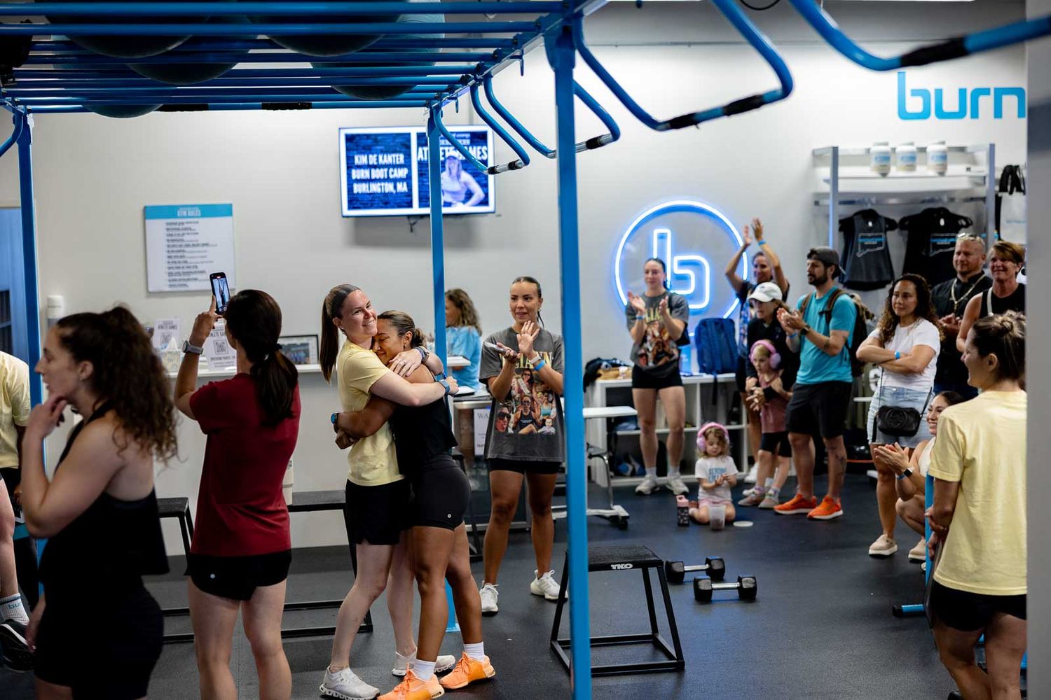 Group fitness class participants gather in a gym space with distinctive blue overhead equipment.