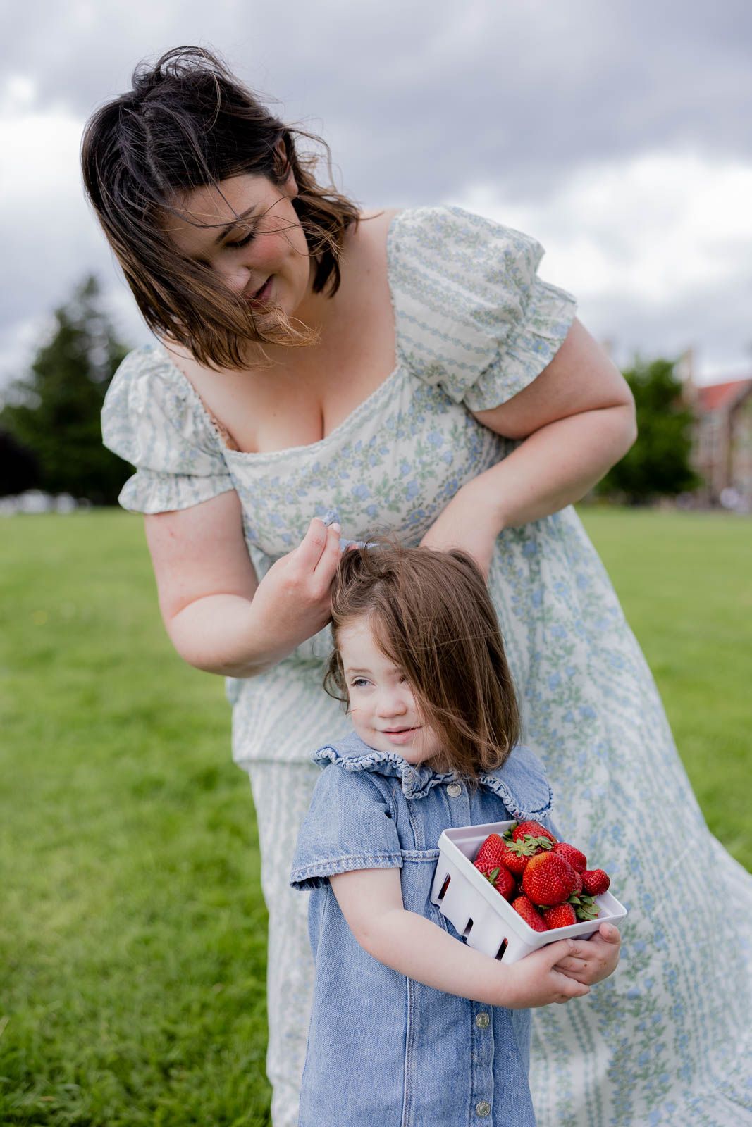 A family picnic moment on a grassy field with a floral dress and denim overalls.